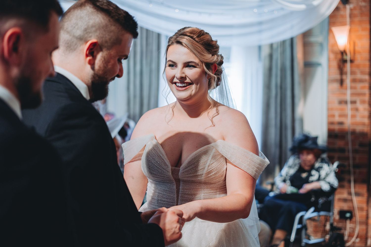 Intimate wedding ceremony moment inside a rustic brick-walled venue with blue draping.