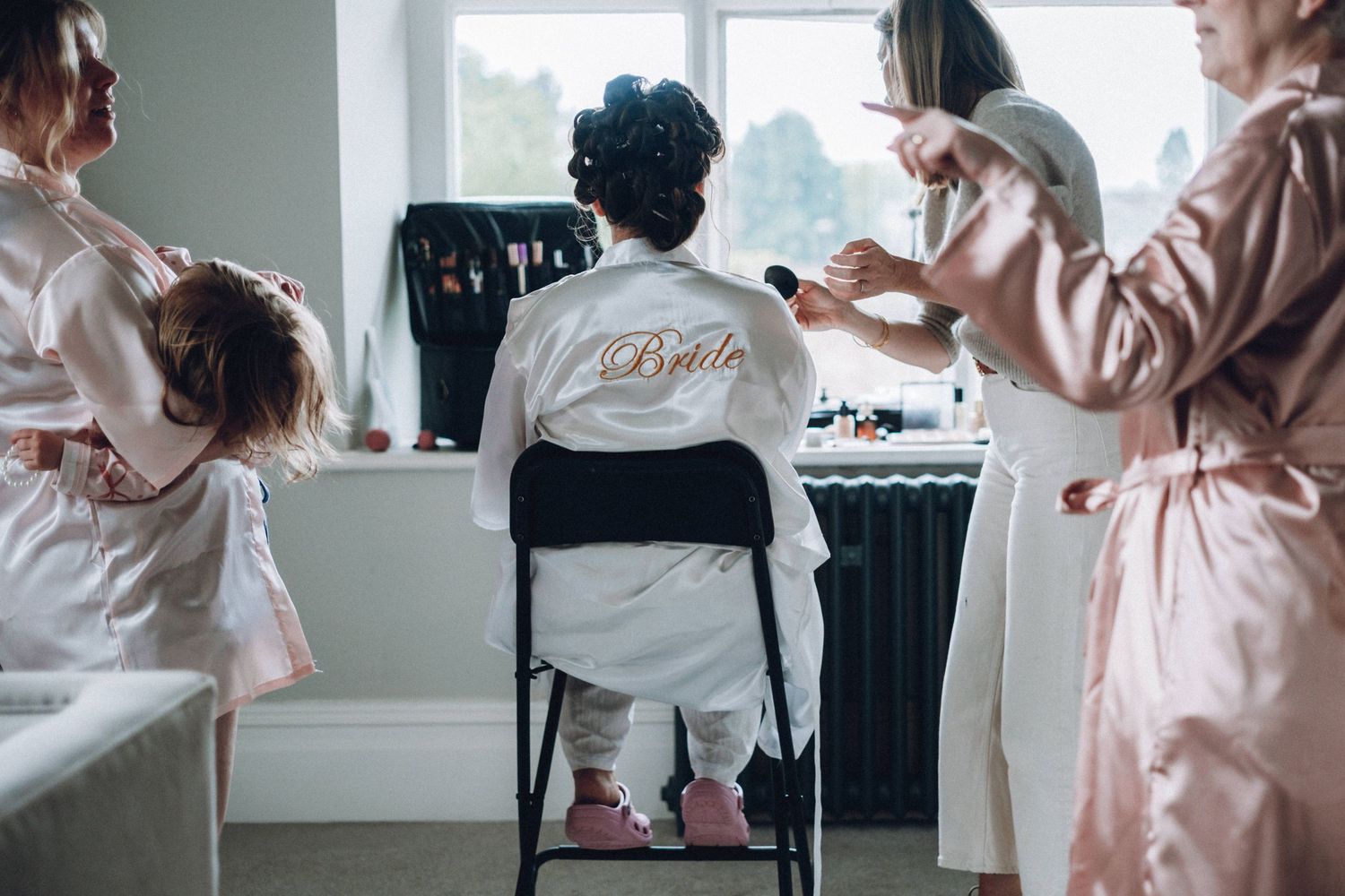 Wedding morning preparations with multiple people in white and pink robes.