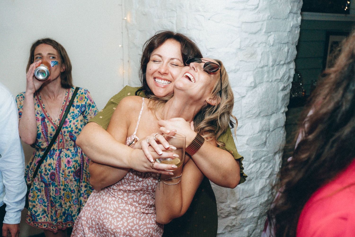 Joyful celebration moments captured during a wedding reception with white brick wall background.