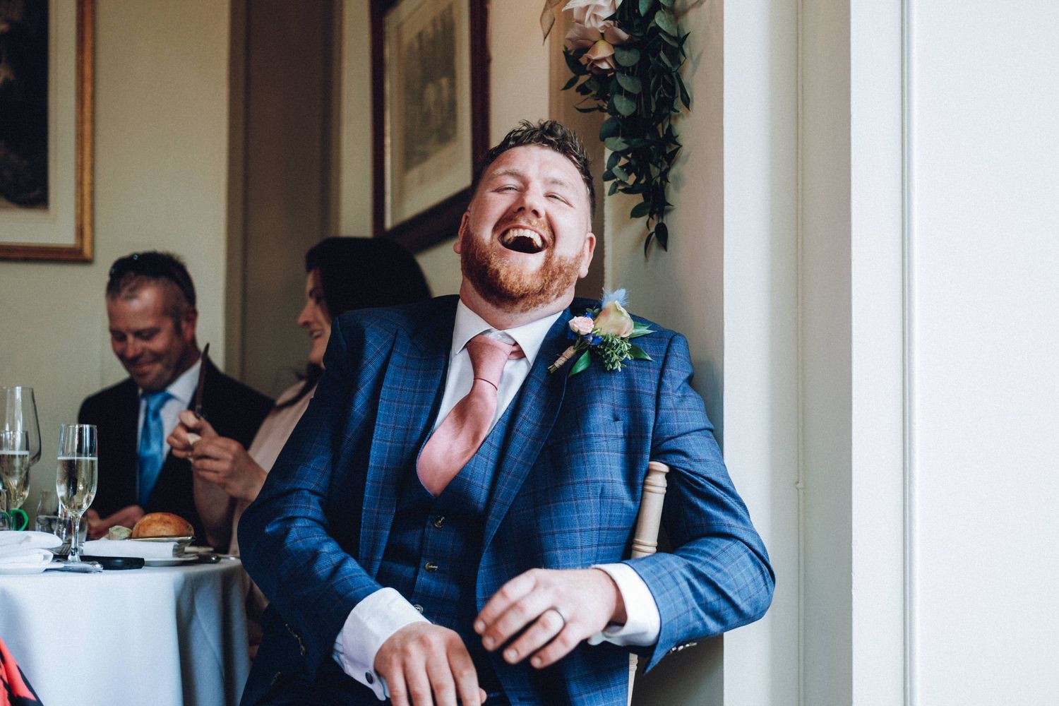 Wedding party in navy suits sharing laughs during indoor celebration.