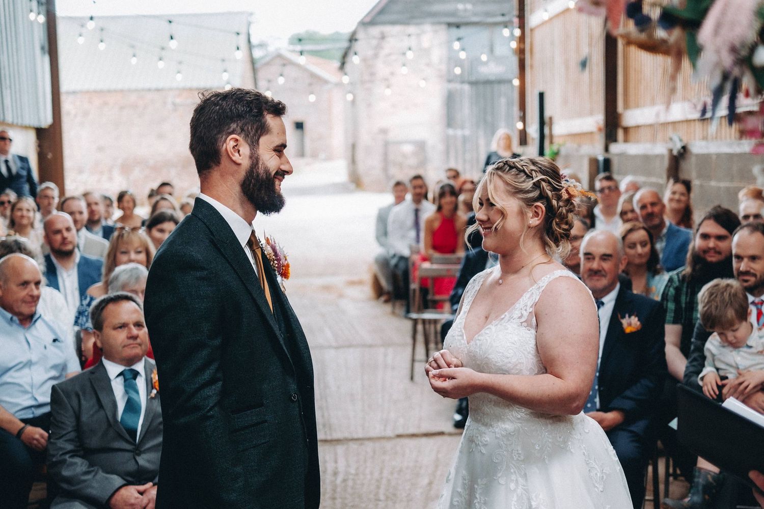 A couple exchanges vows during an intimate wedding ceremony in front of seated guests in a rustic outdoor venue.
