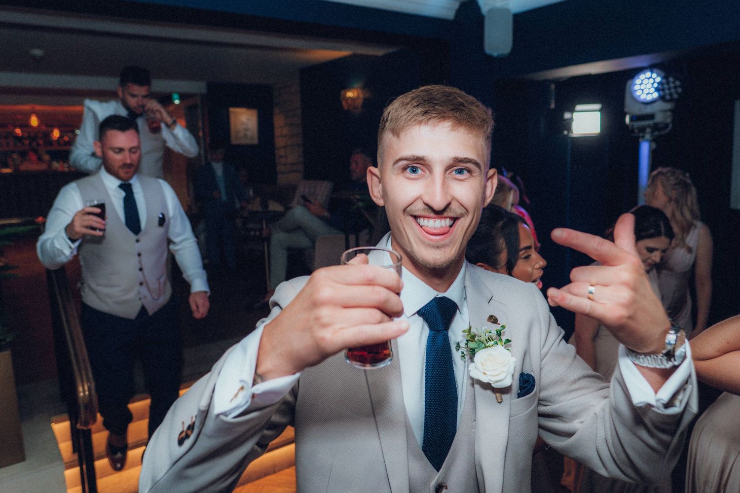 A celebratory moment at a wedding reception as someone in a light gray suit makes a toast with a drink.