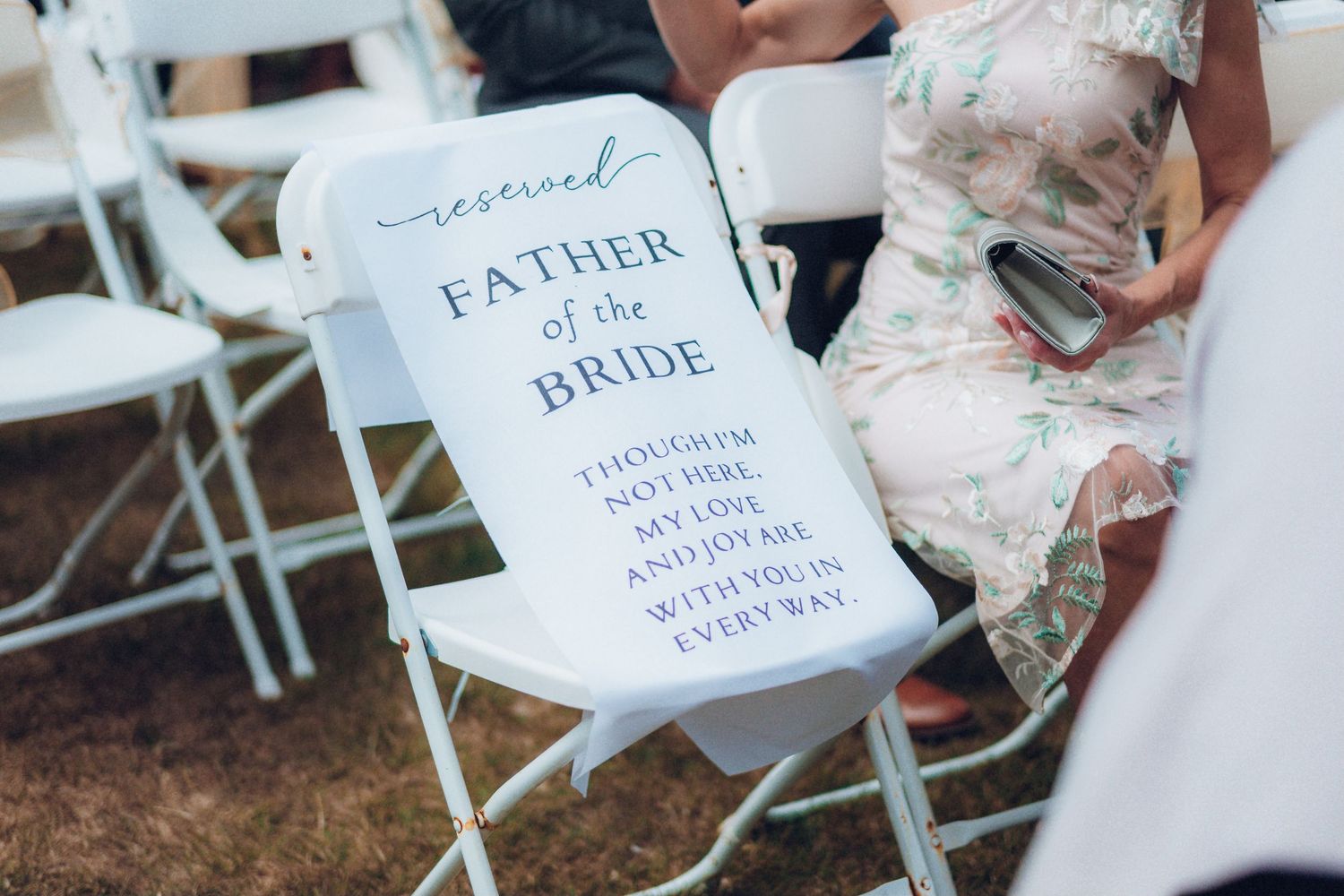Elegant wedding ceremony signage displayed on white chairs in an outdoor setting.