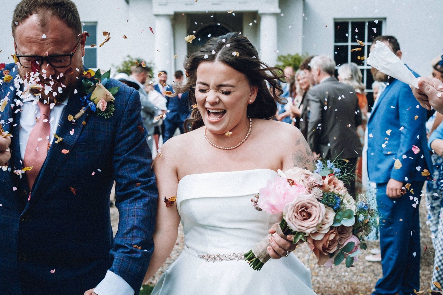 Wedding celebration with confetti being thrown as couple walks through crowd of guests.