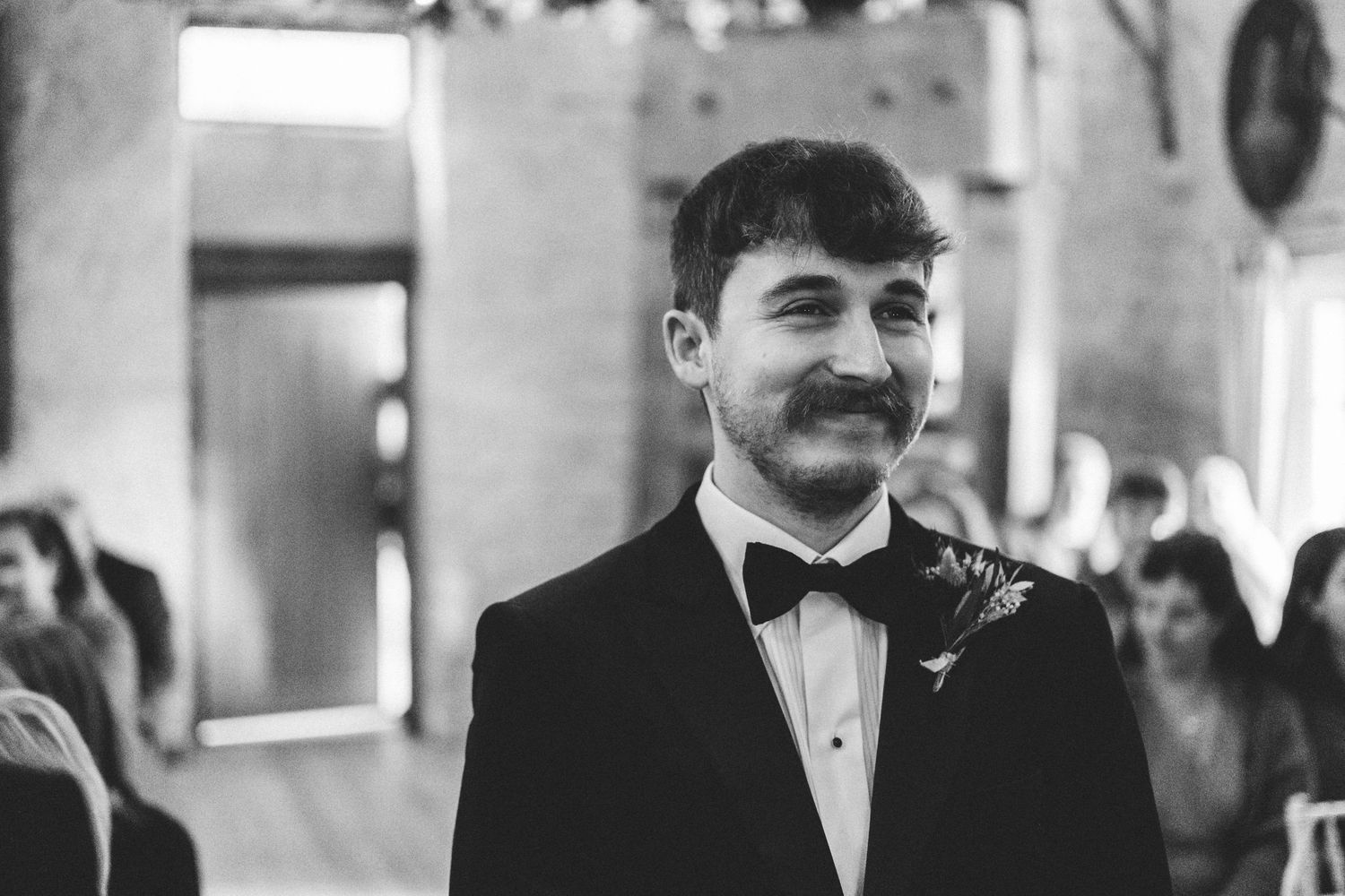 A person in a black bow tie and tuxedo smiles during a wedding celebration.
