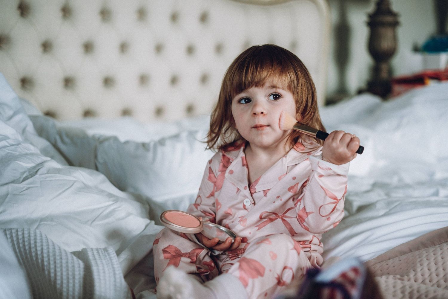 Young child in pink floral dress relaxing on tufted headboard bed.