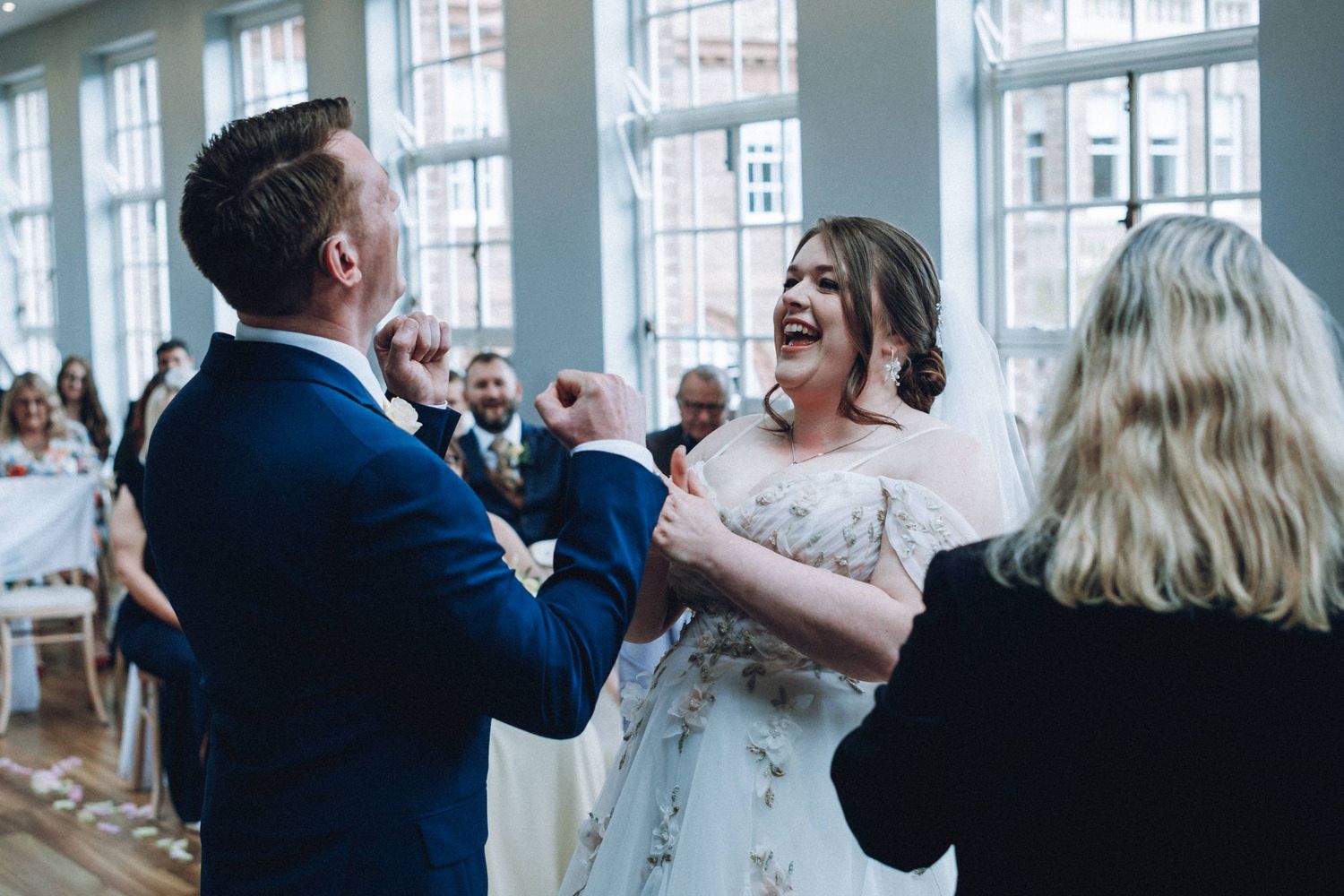 Wedding celebration in bright indoor venue with large windows and dancing guests.