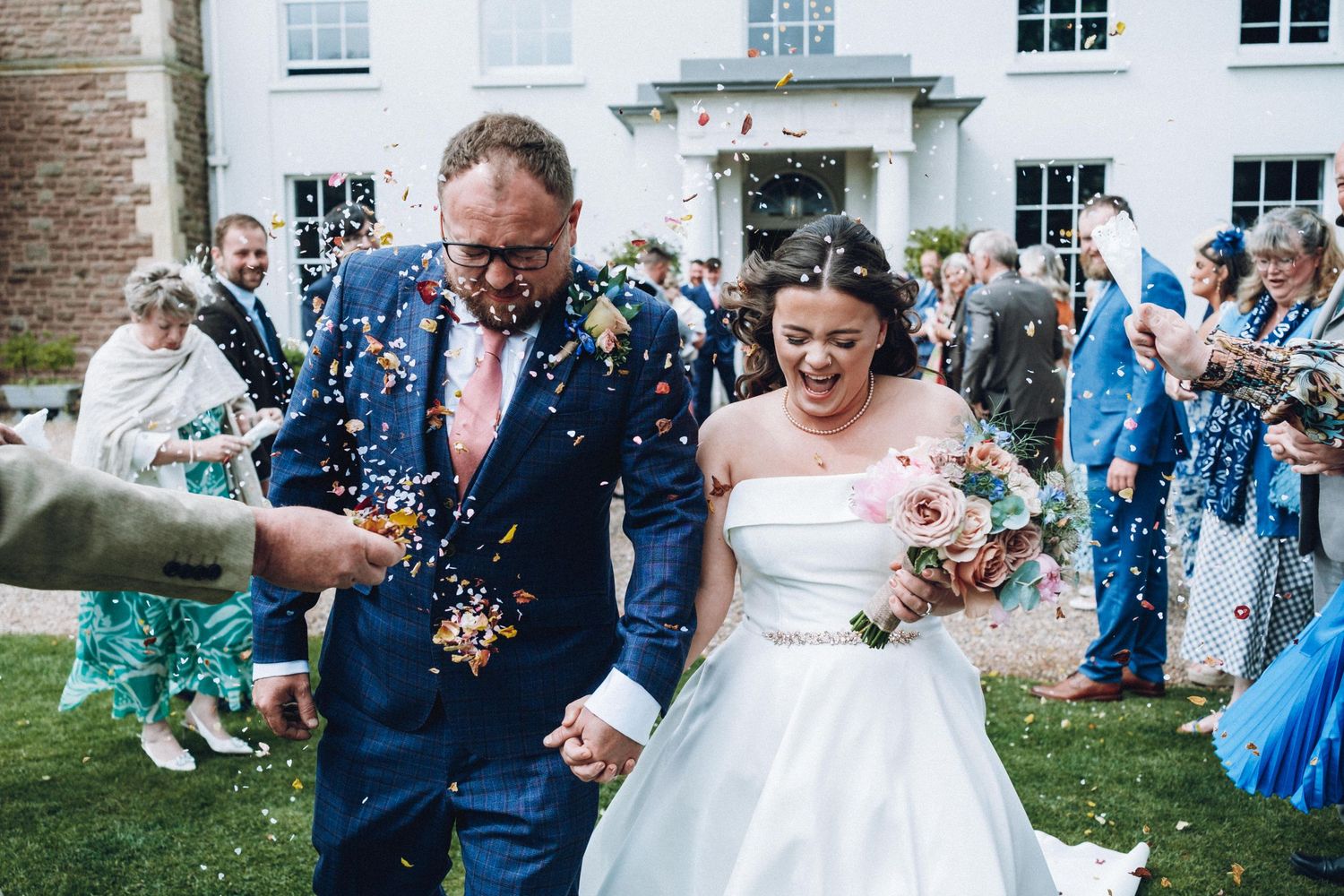 Joyful wedding party and guests celebrate with confetti on the lawn.