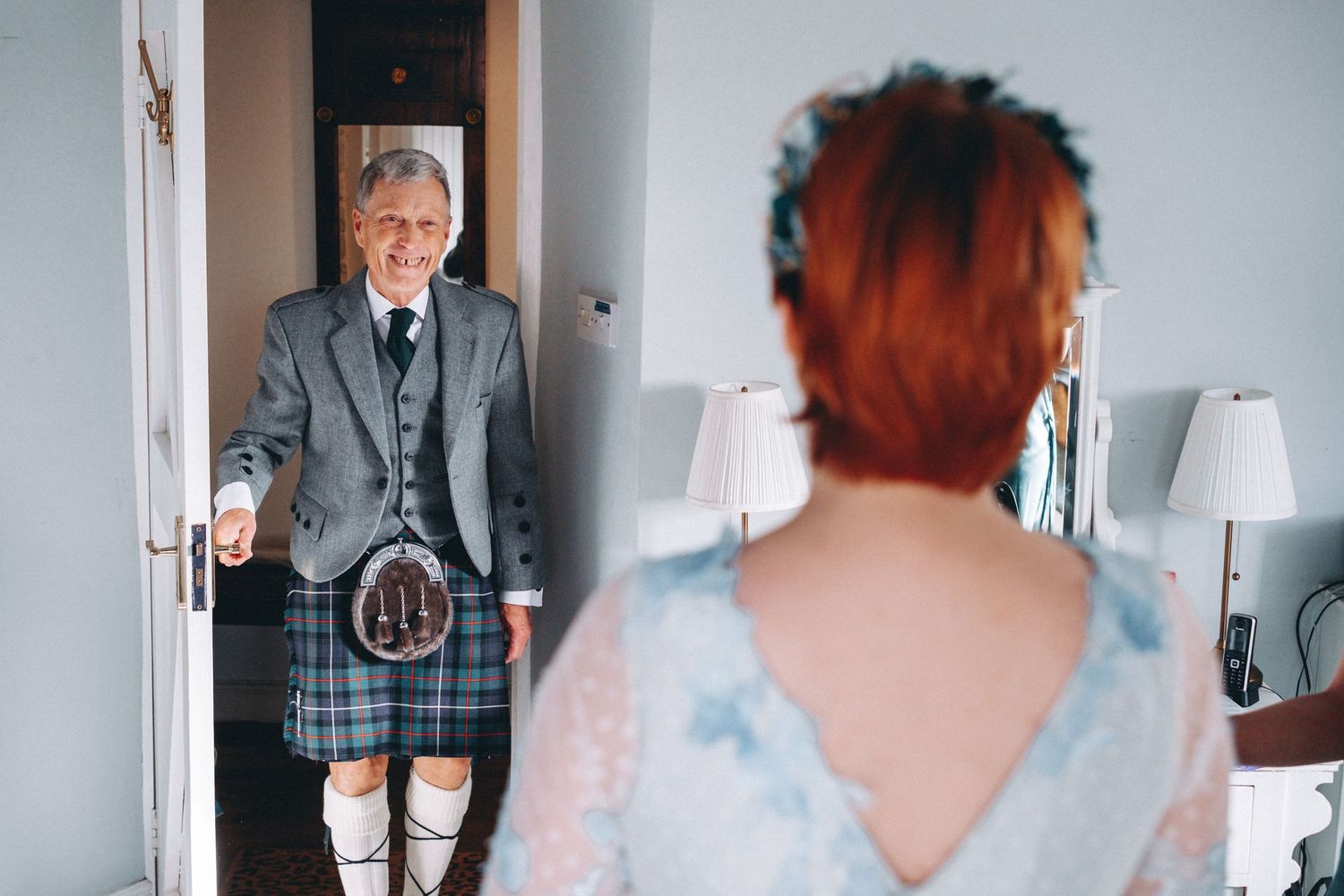 Scottish groom in traditional kilt appears in doorway during wedding preparations.