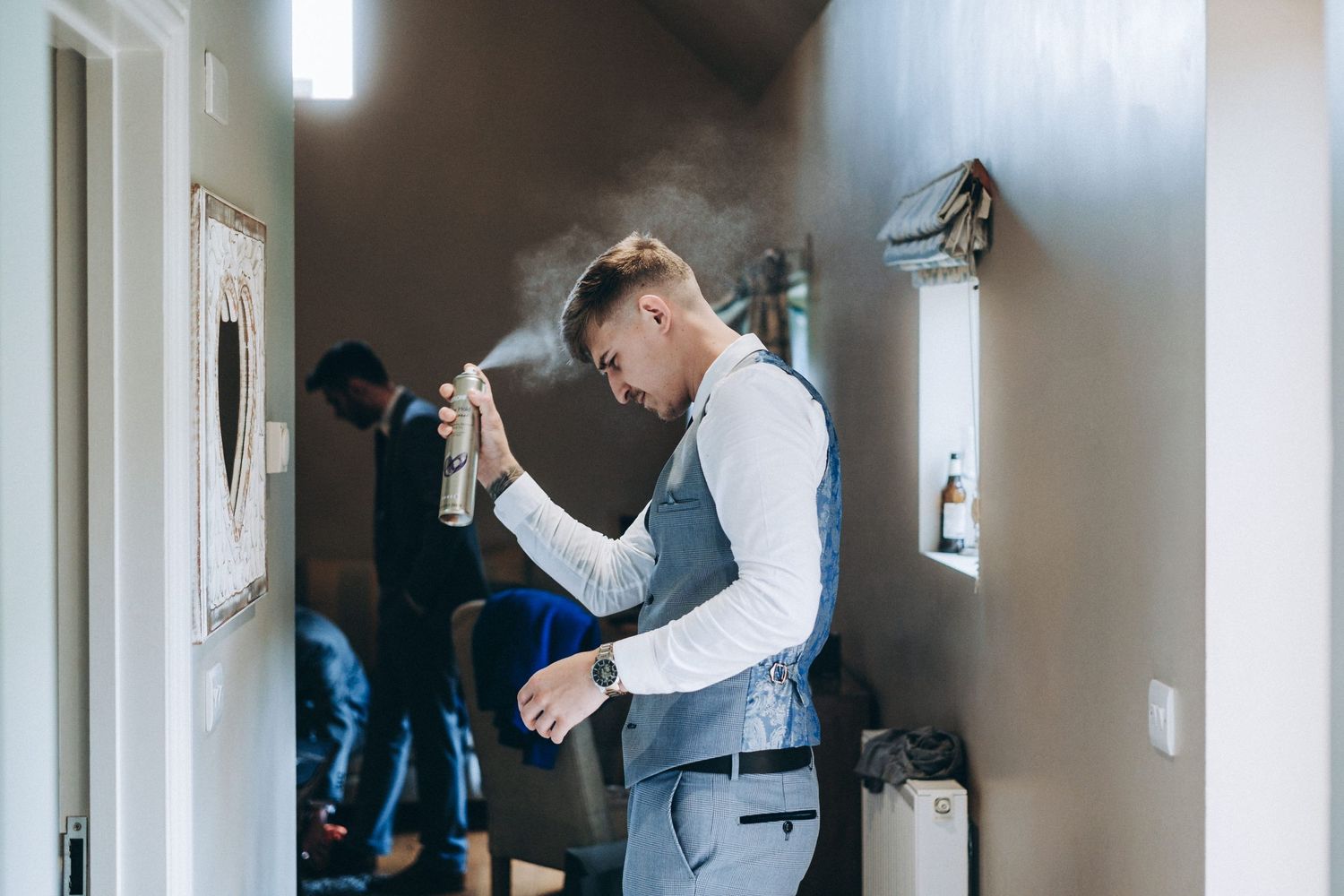 Groomsmen prepares in a hallway before wedding with others visible in the background.