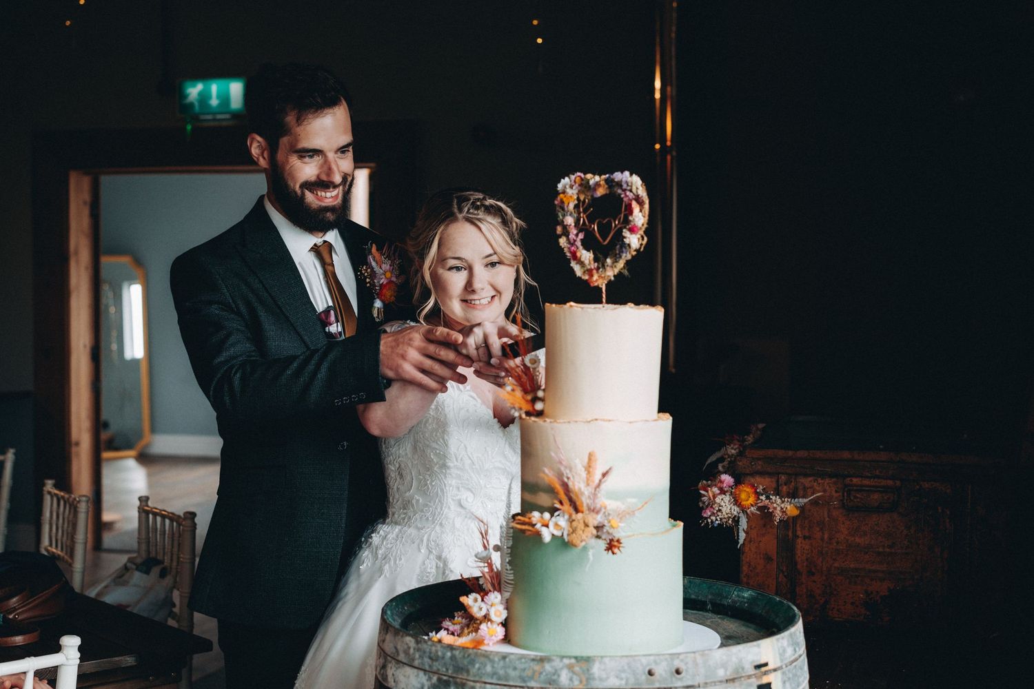 A bride and groom cutting into their elegant three-tier mint and white wedding cake with a gold topper.