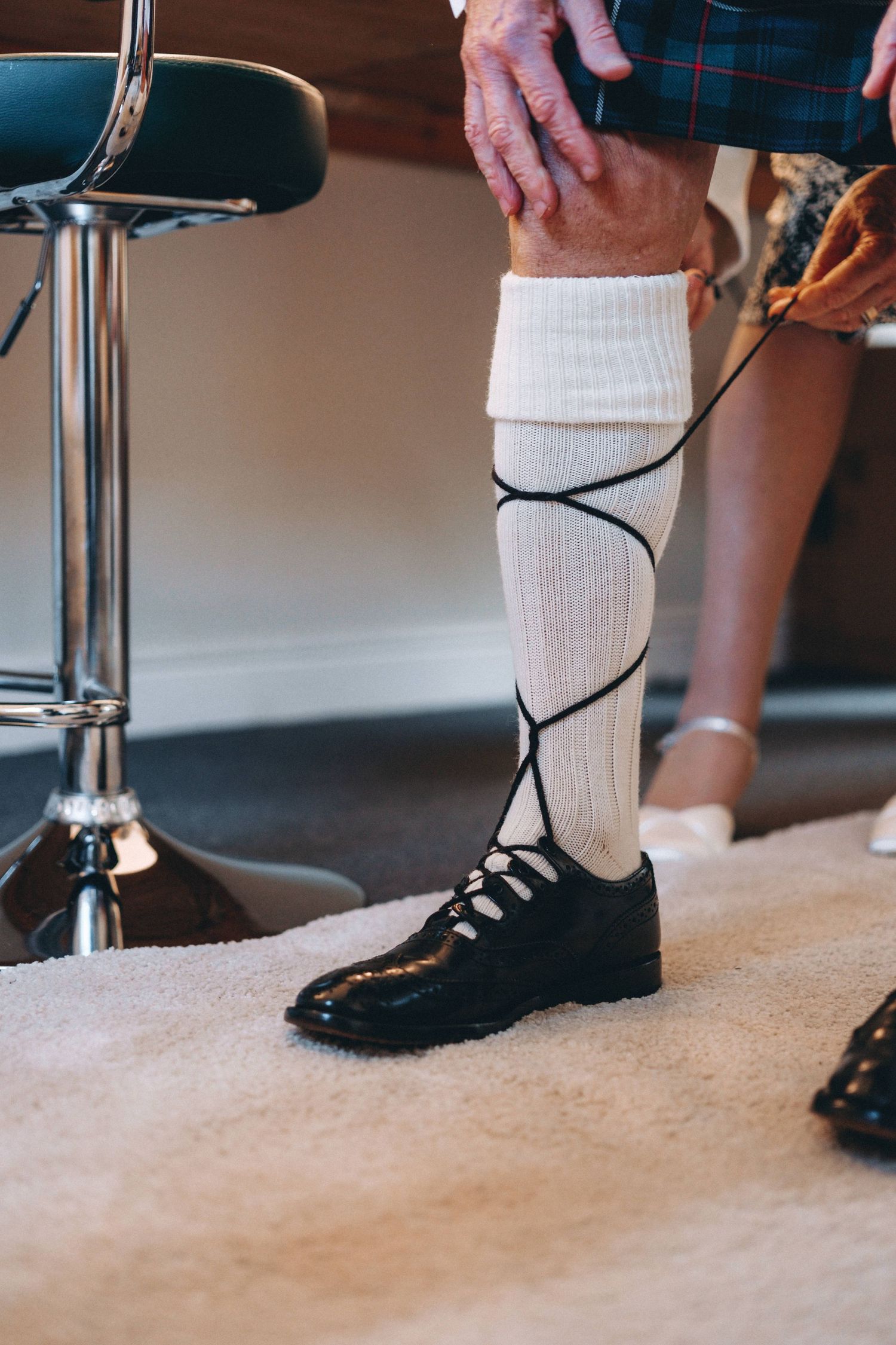 Close-up of traditional Scottish kilt socks and dress shoes being adjusted.