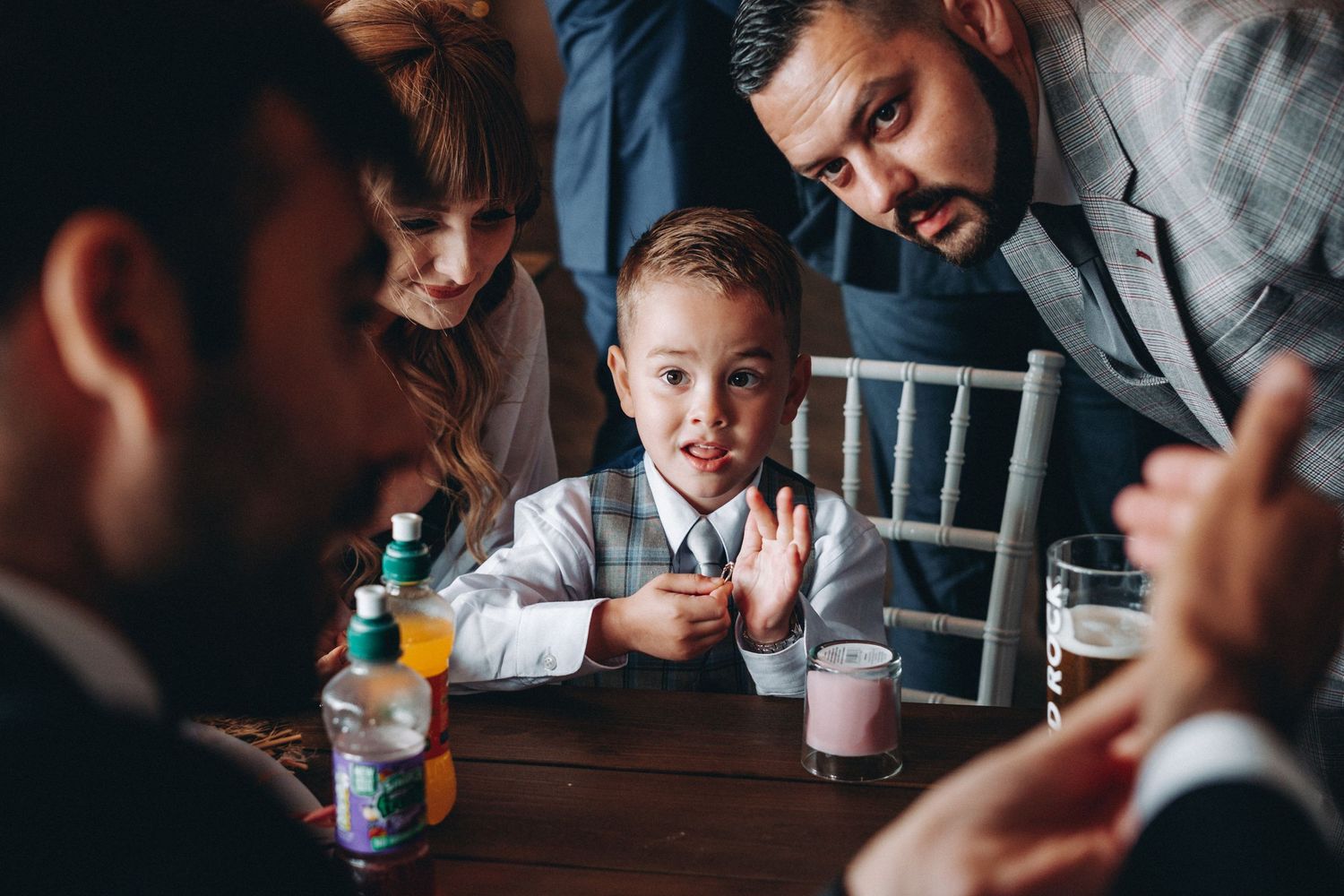 Magician and several people gathered around a wooden table with drinks during a wedding.