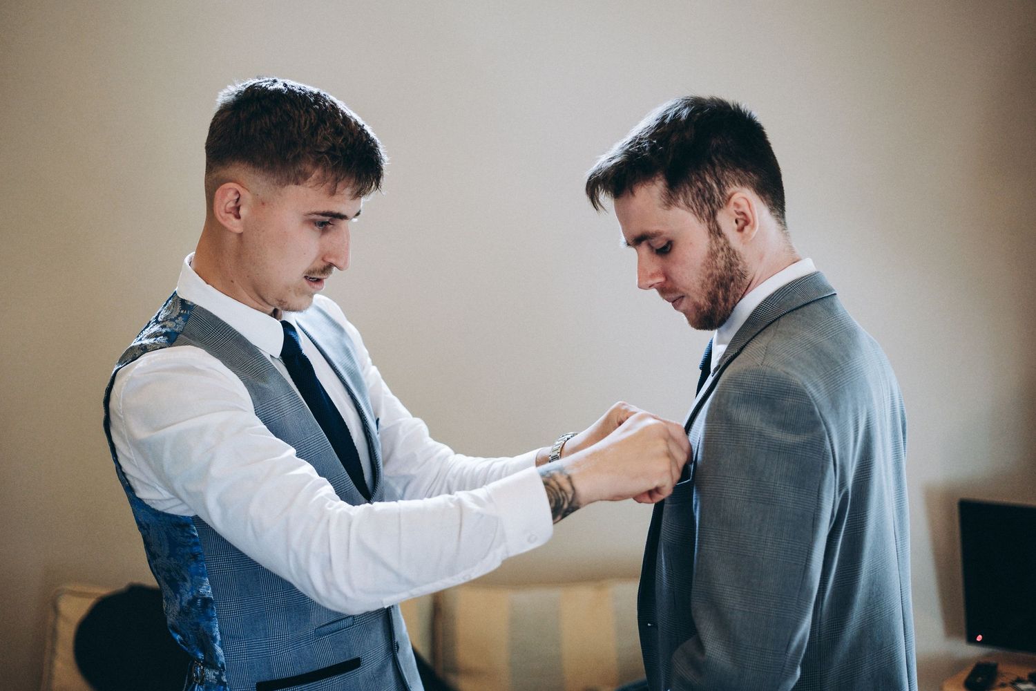 groomsmen in wedding attire help each other prepare, adjusting clothing details.