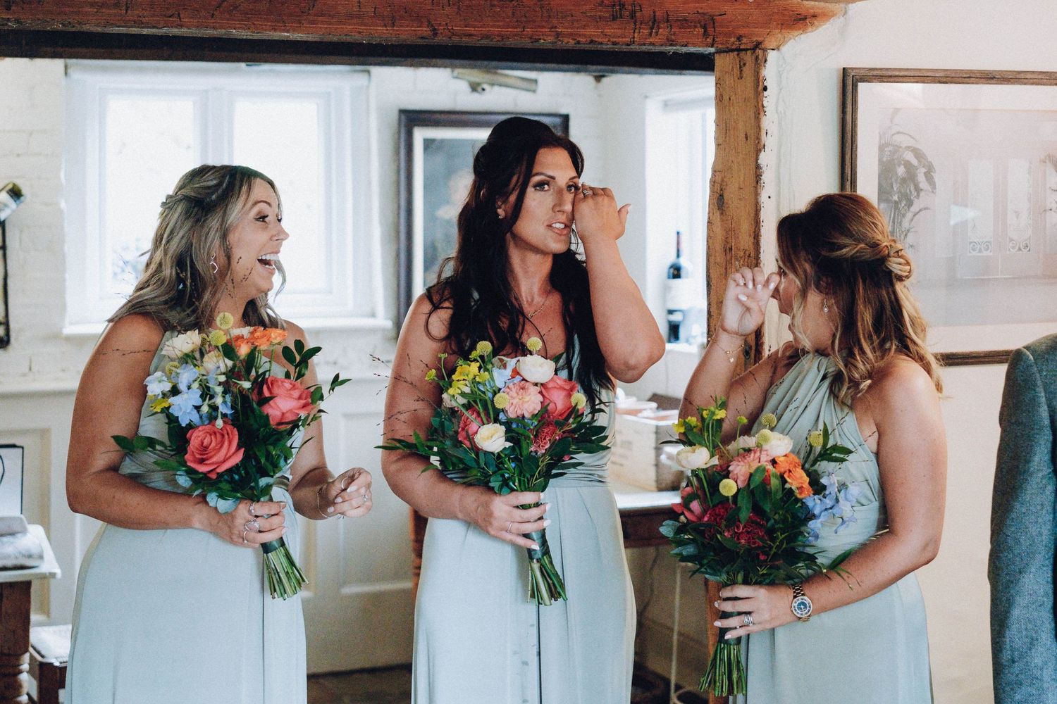 Three bridesmaids in mint green dresses holding colorful floral bouquets.