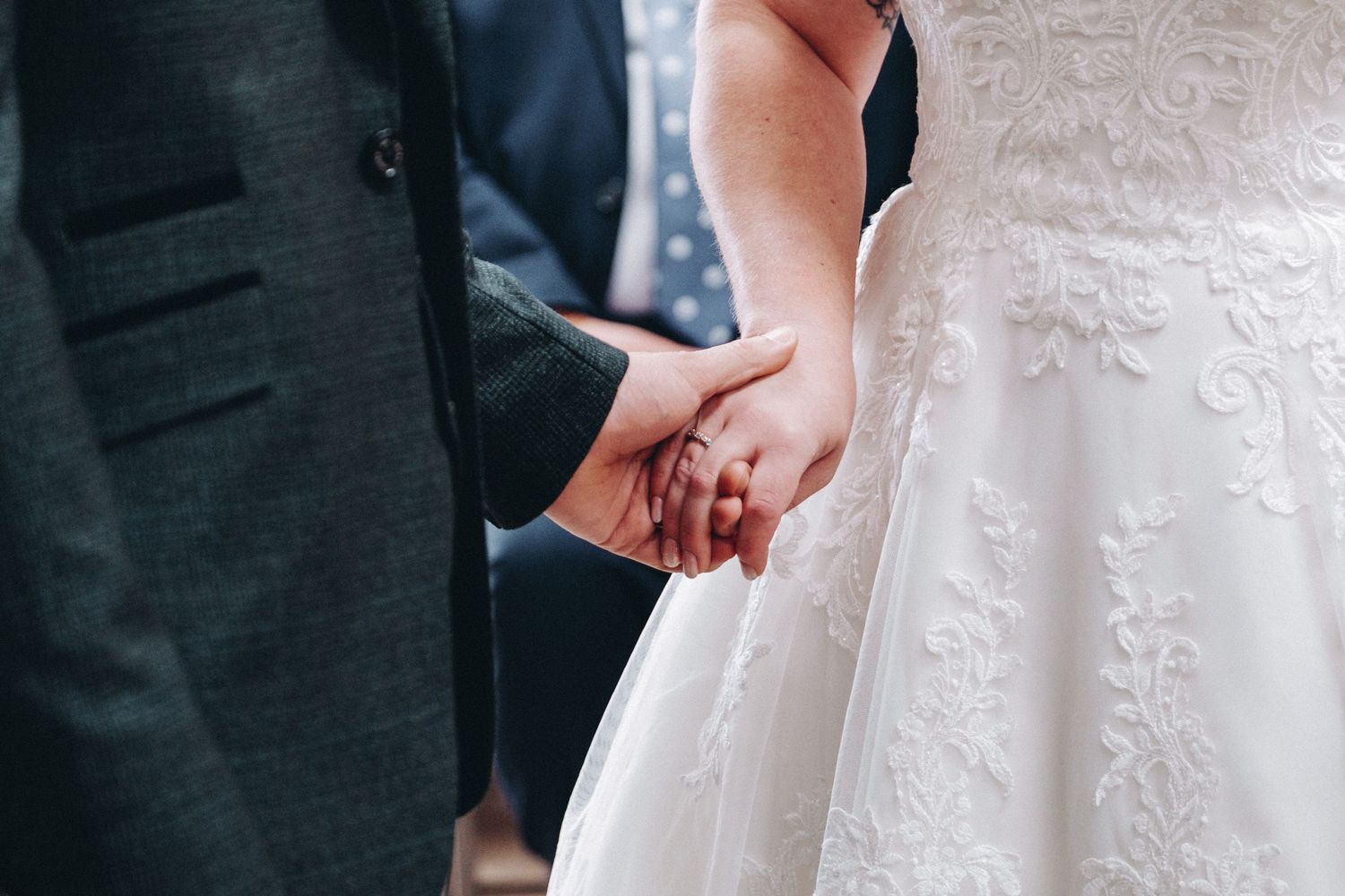 Close-up shot of a couple holding hands during their wedding ceremony, showing elegant dress and suit details.