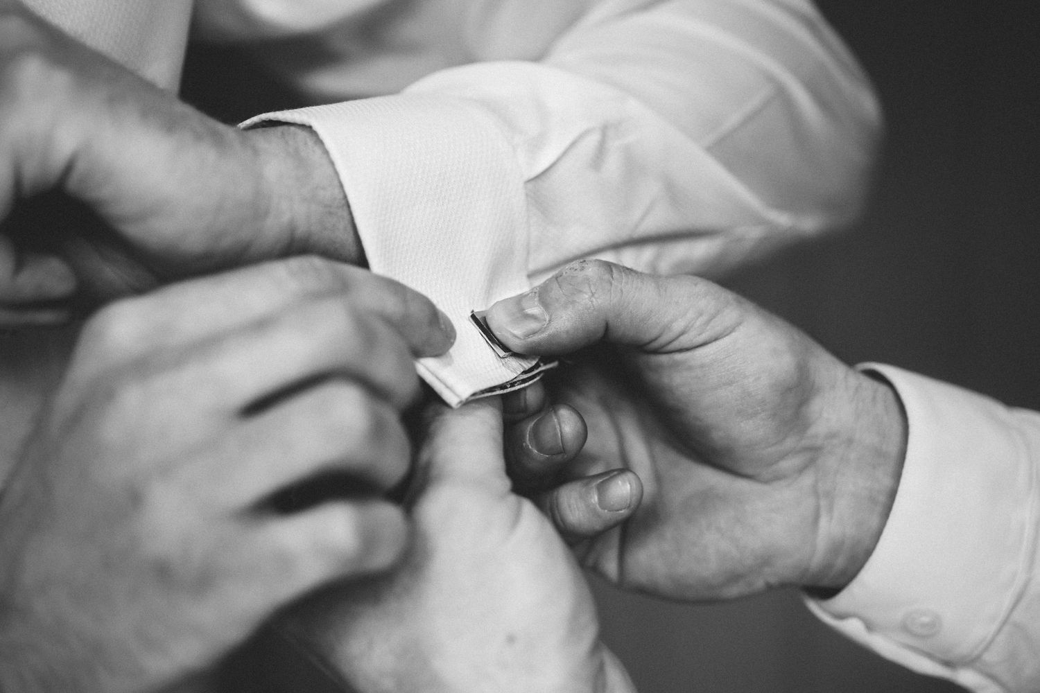 Close-up black and white shot of hands adjusting formal wedding attire details.