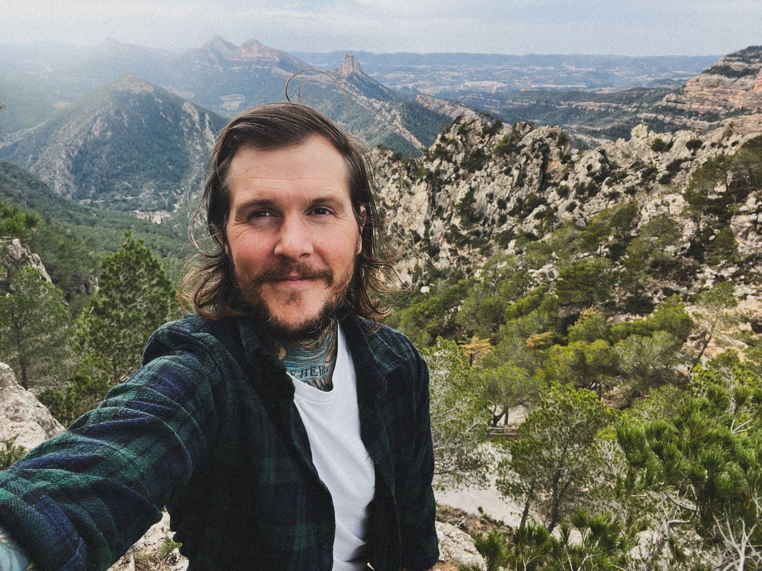 Selfie taken on mountain trail with vast wilderness landscape in background.