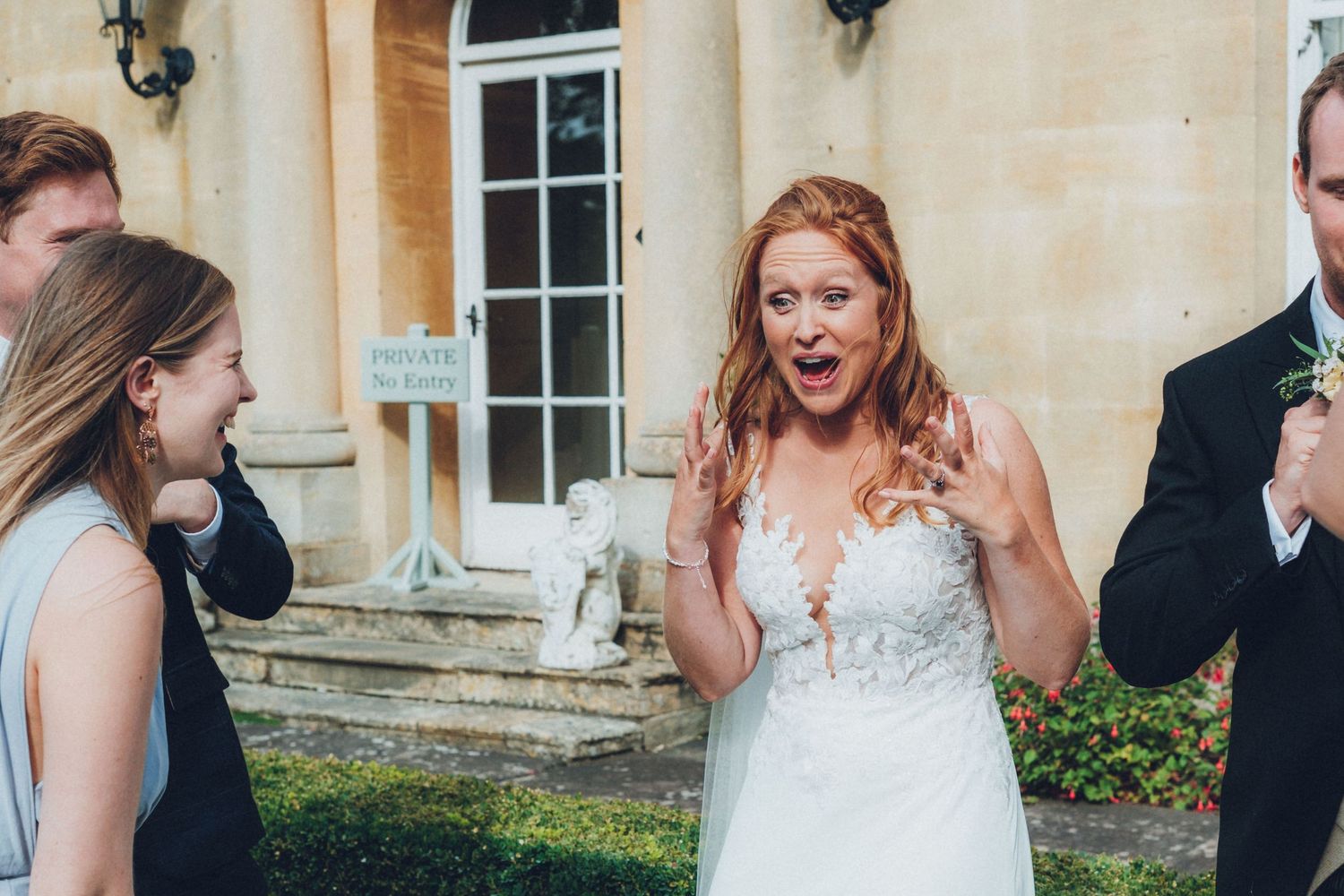 Wedding party poses and laughs outside elegant stone building.