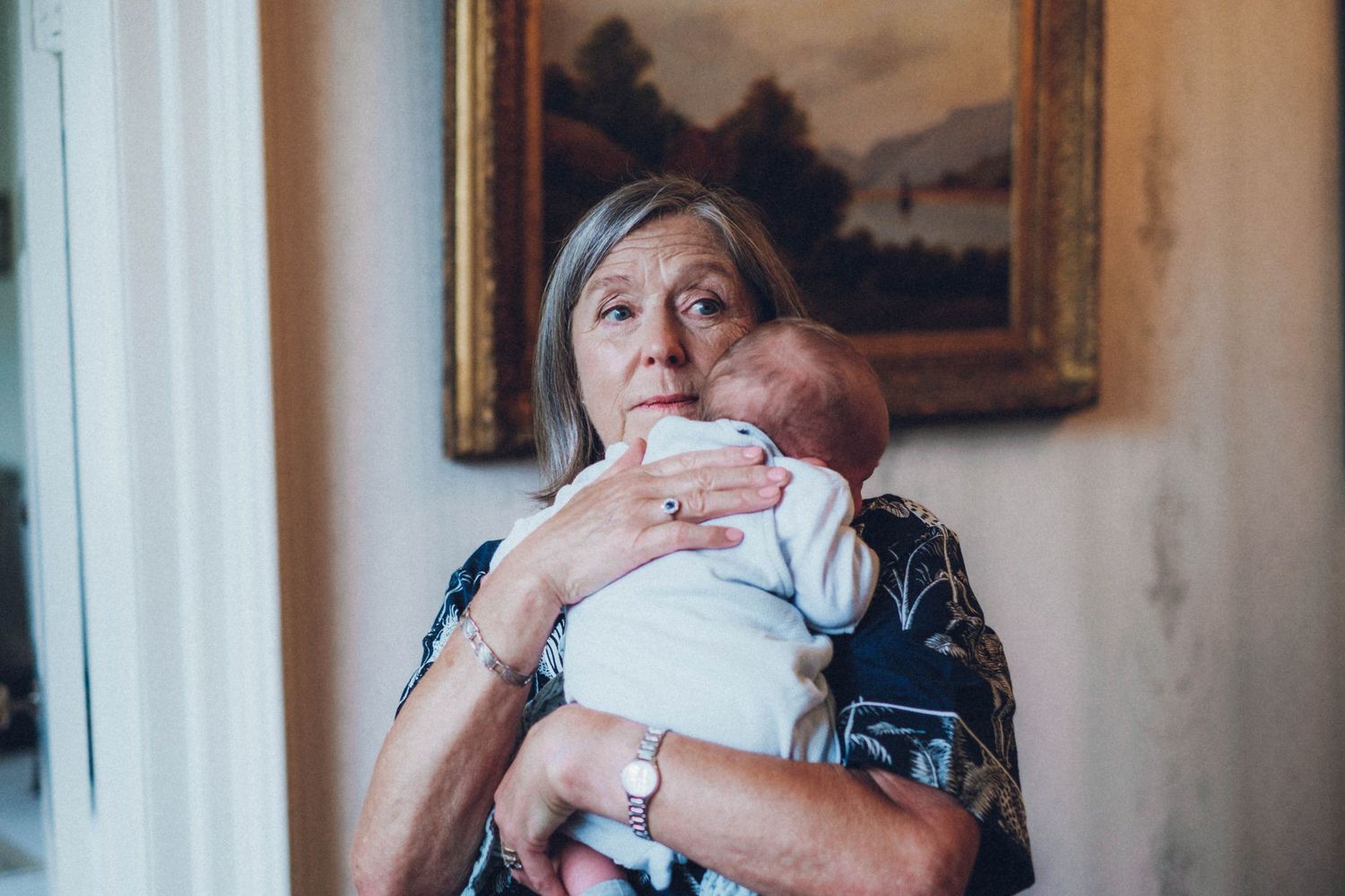 A tender moment captured between a baby and caregiver near a window with artwork in background.