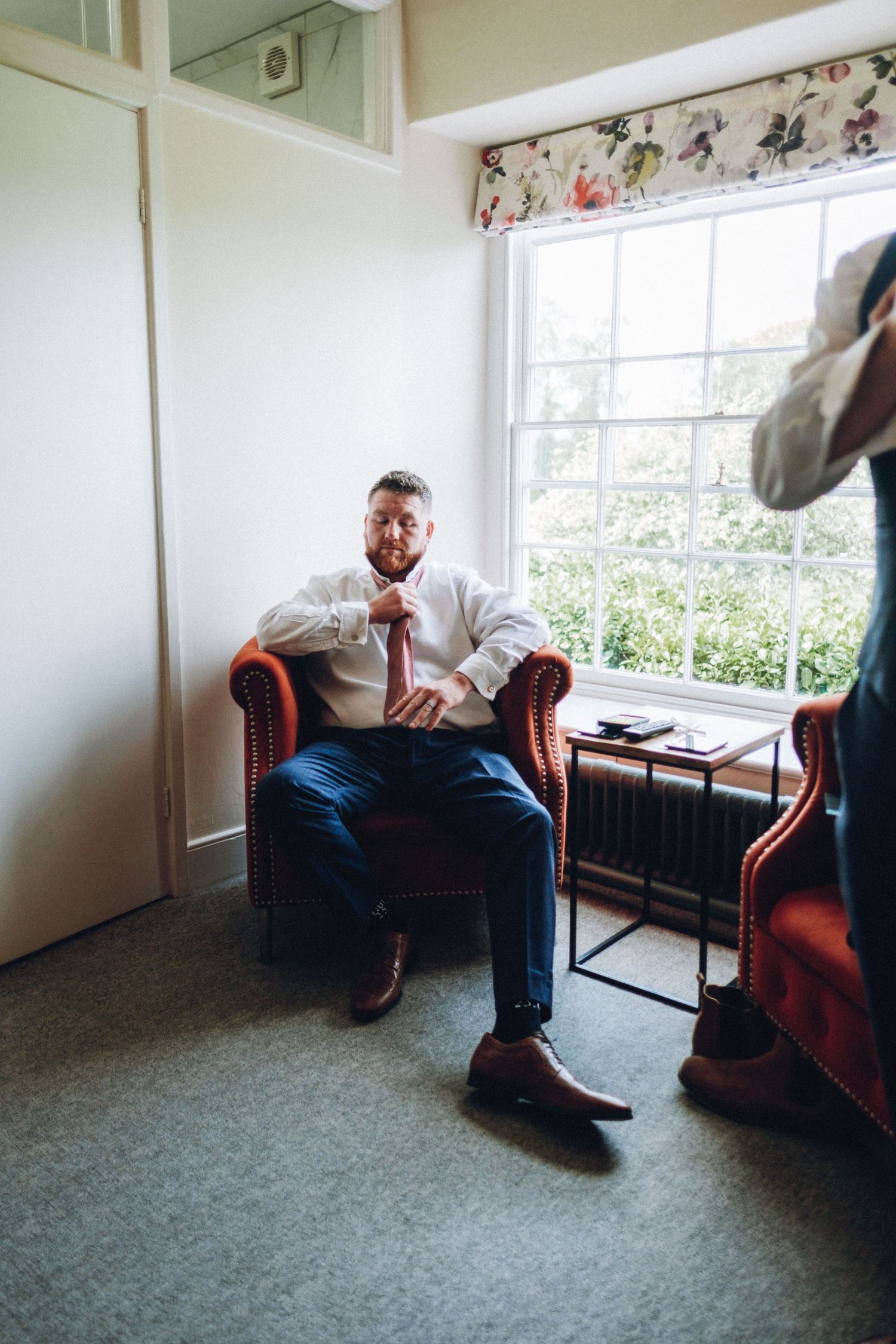 Person sitting on red armchair in bright room with windows.