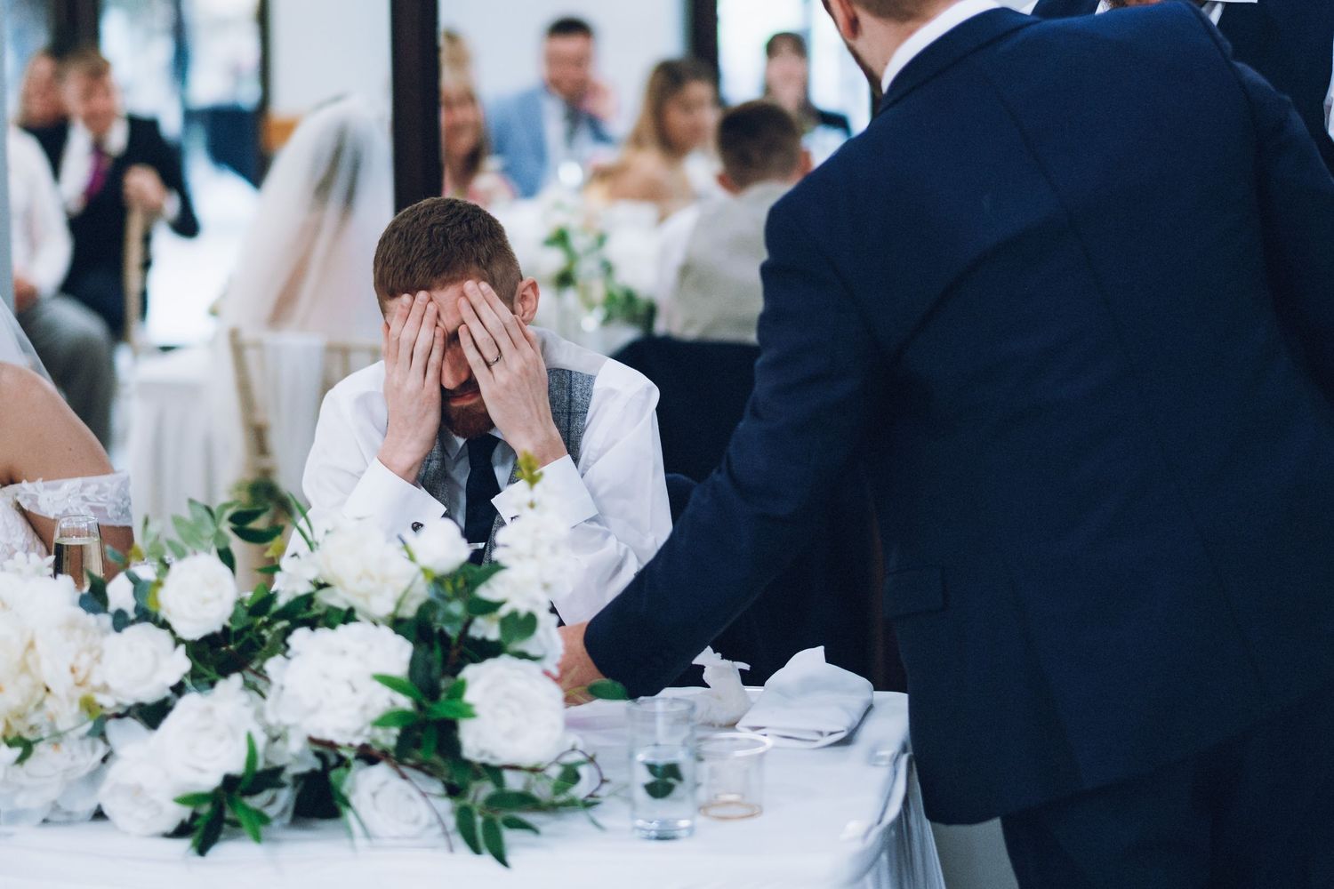 An emotional moment captured at an elegantly decorated wedding reception table with white floral arrangements.