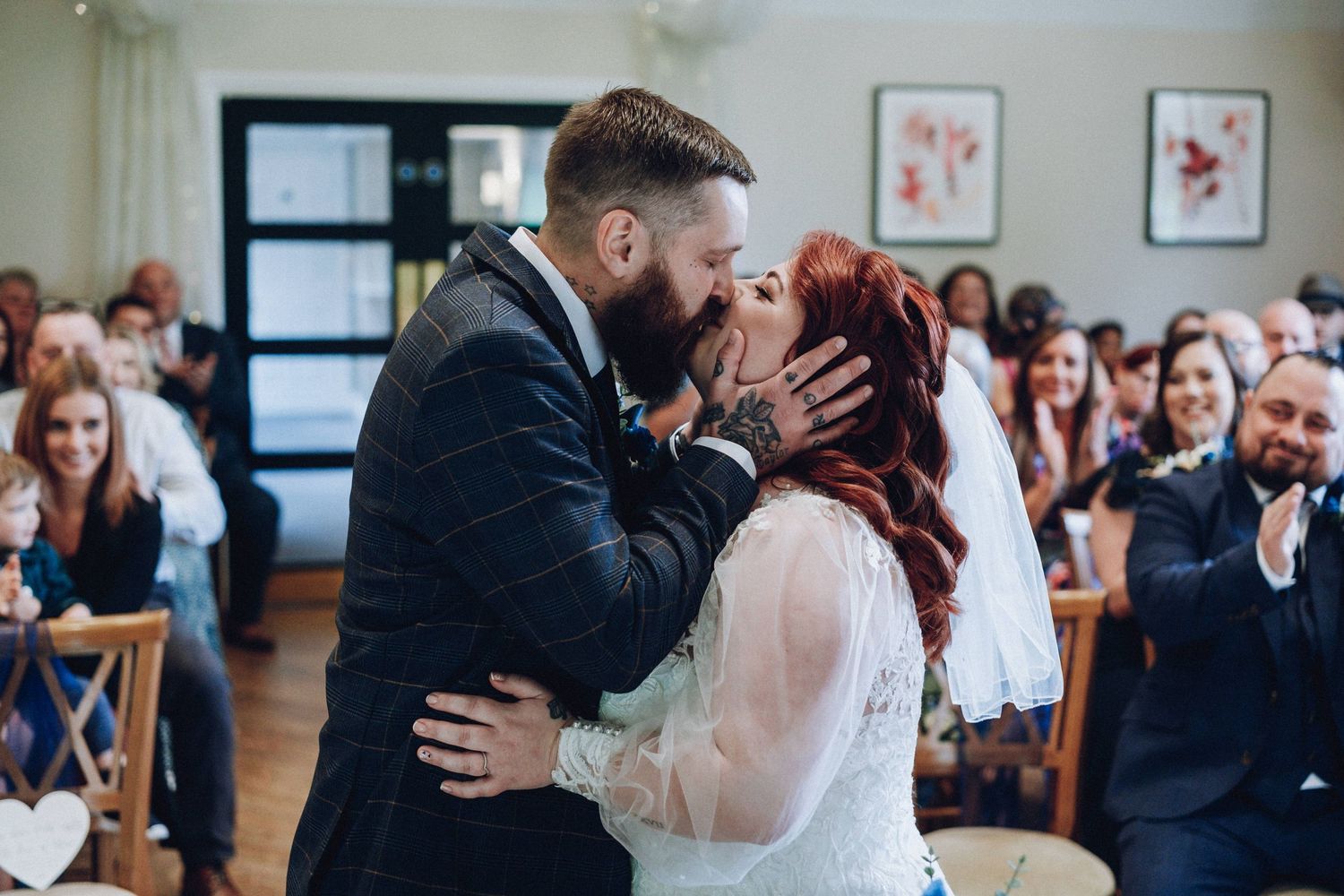 Wedding ceremony guests gather in a bright indoor venue with decorative wall art.