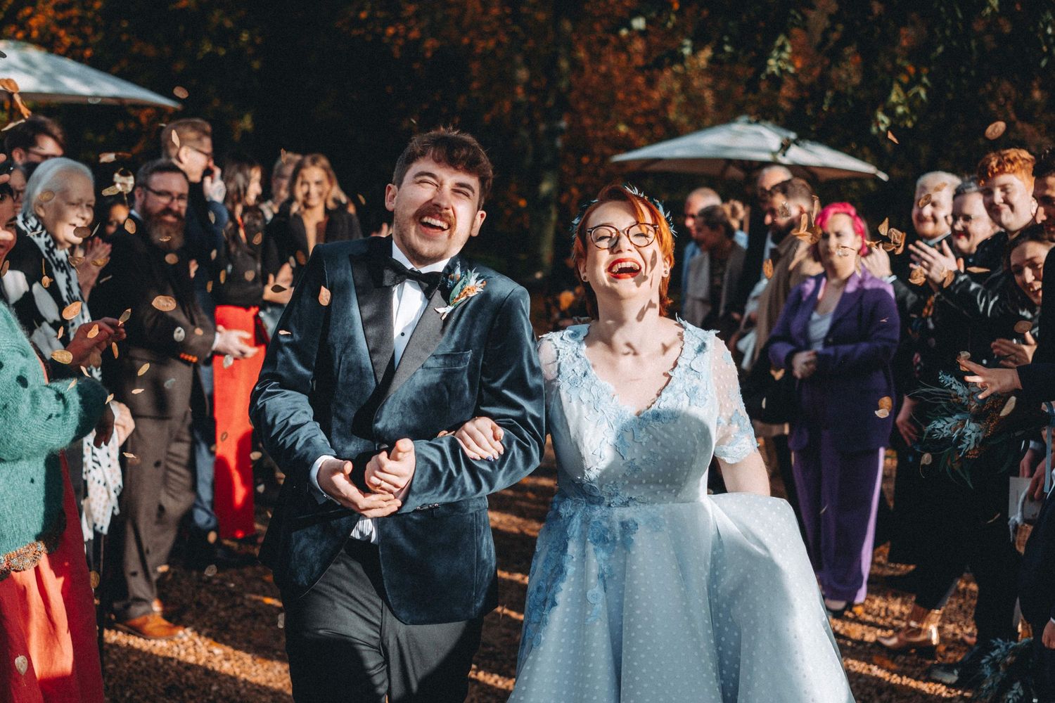 Wedding celebration outdoors at night with guests smiling and cheering as couple walks through crowd.