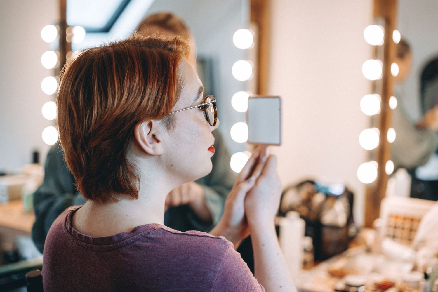 Bride looks into mirror with vanity lights in makeup room at Owlpen Manor.