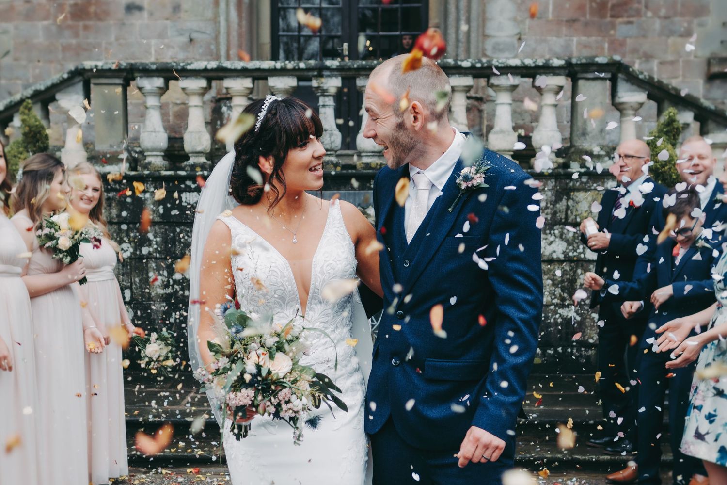Wedding couple celebrates amidst shower of confetti outside historic stone building.