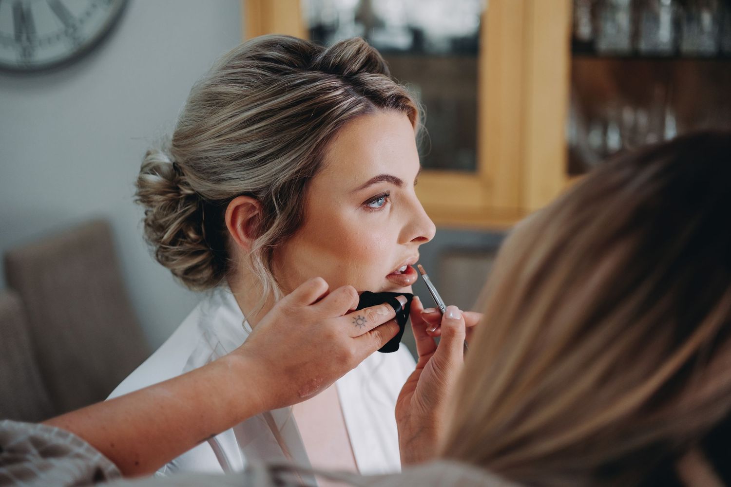 Professional makeup artist applies lipstick to a person in a white robe during wedding preparations.