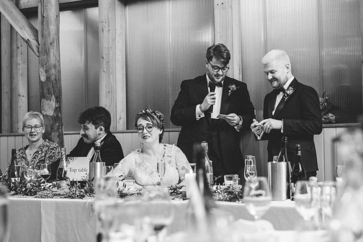 Wedding reception scene in black and white showing formal dinner speeches at the head table.
