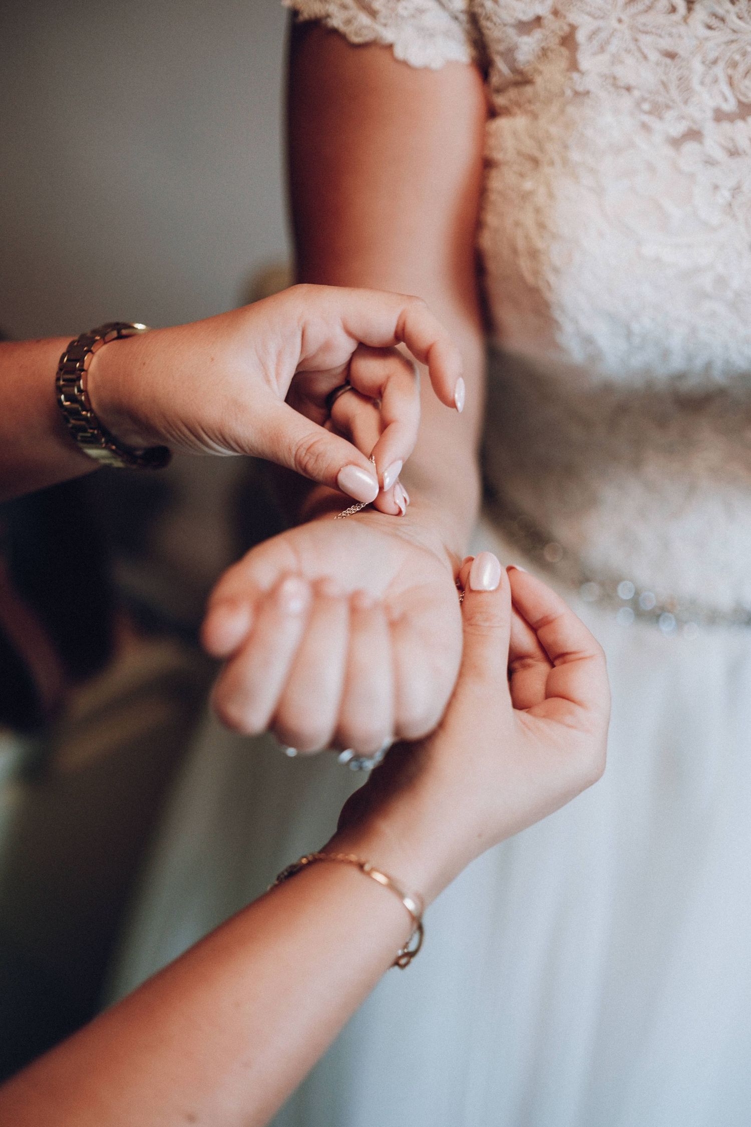 Close-up of hands with bracelets adjusting jewelry against white lace fabric.