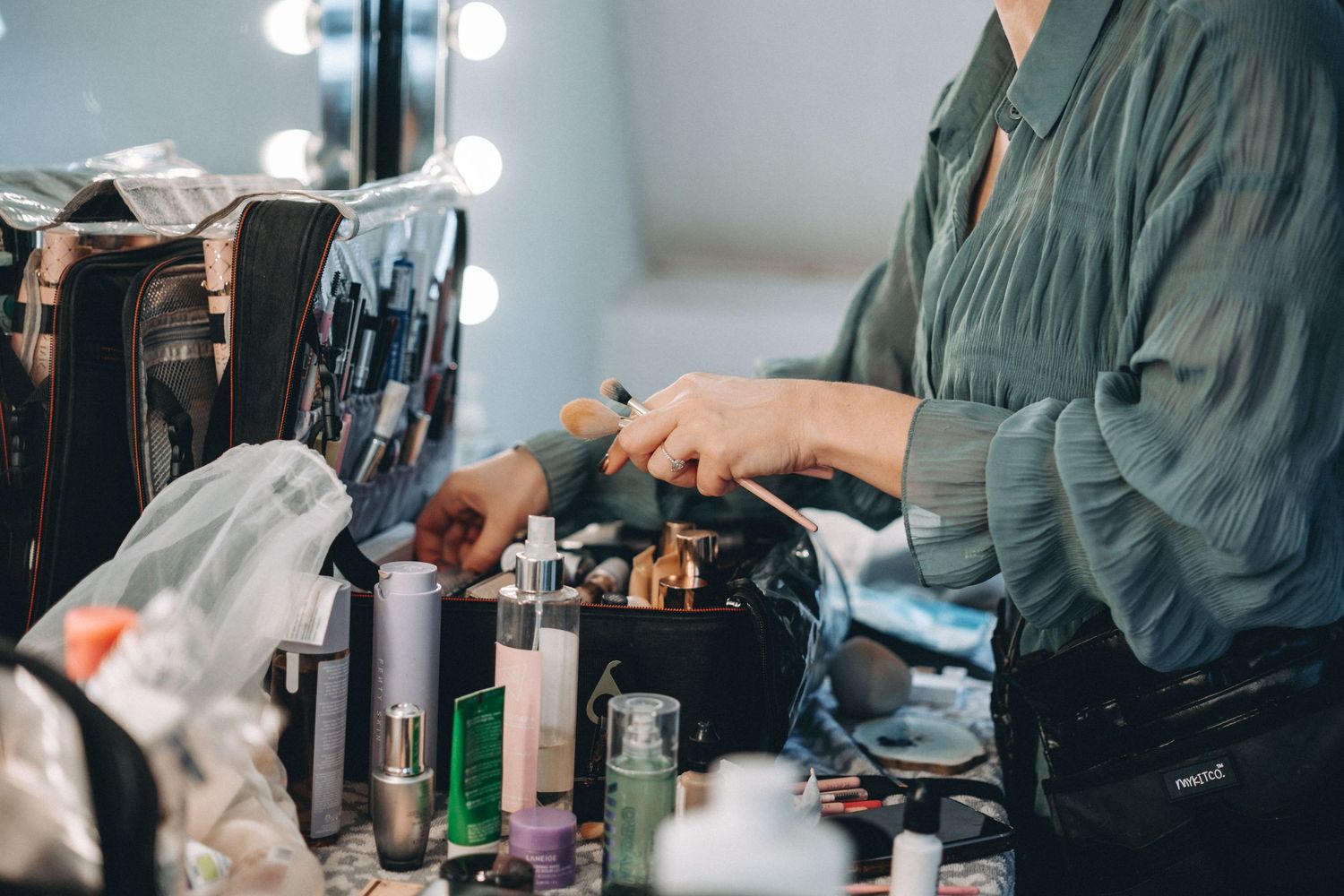 Close-up of beauty products and styling tools on a makeup table with vanity lights.