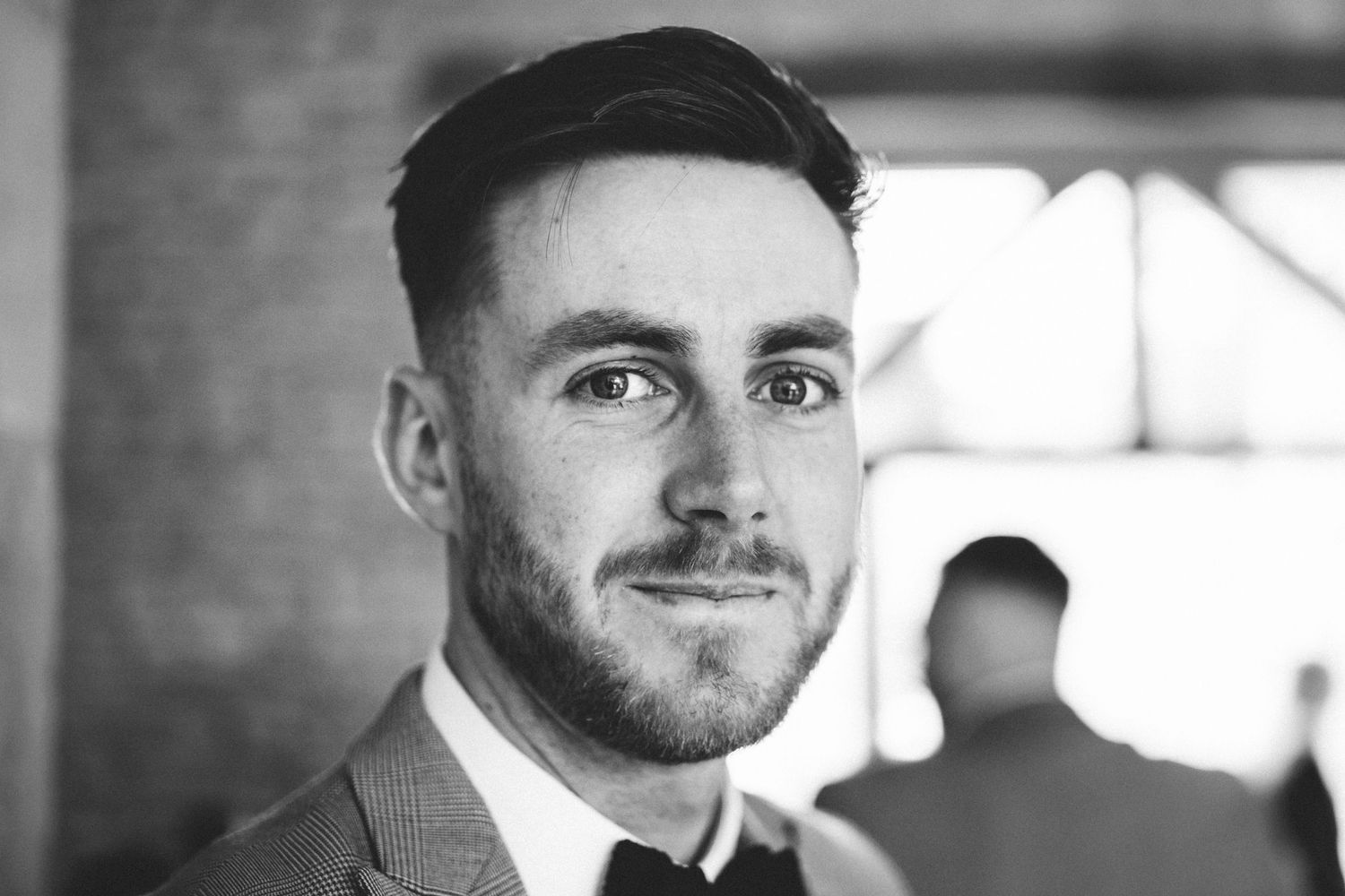 Black and white portrait with soft light and architectural detail in background.