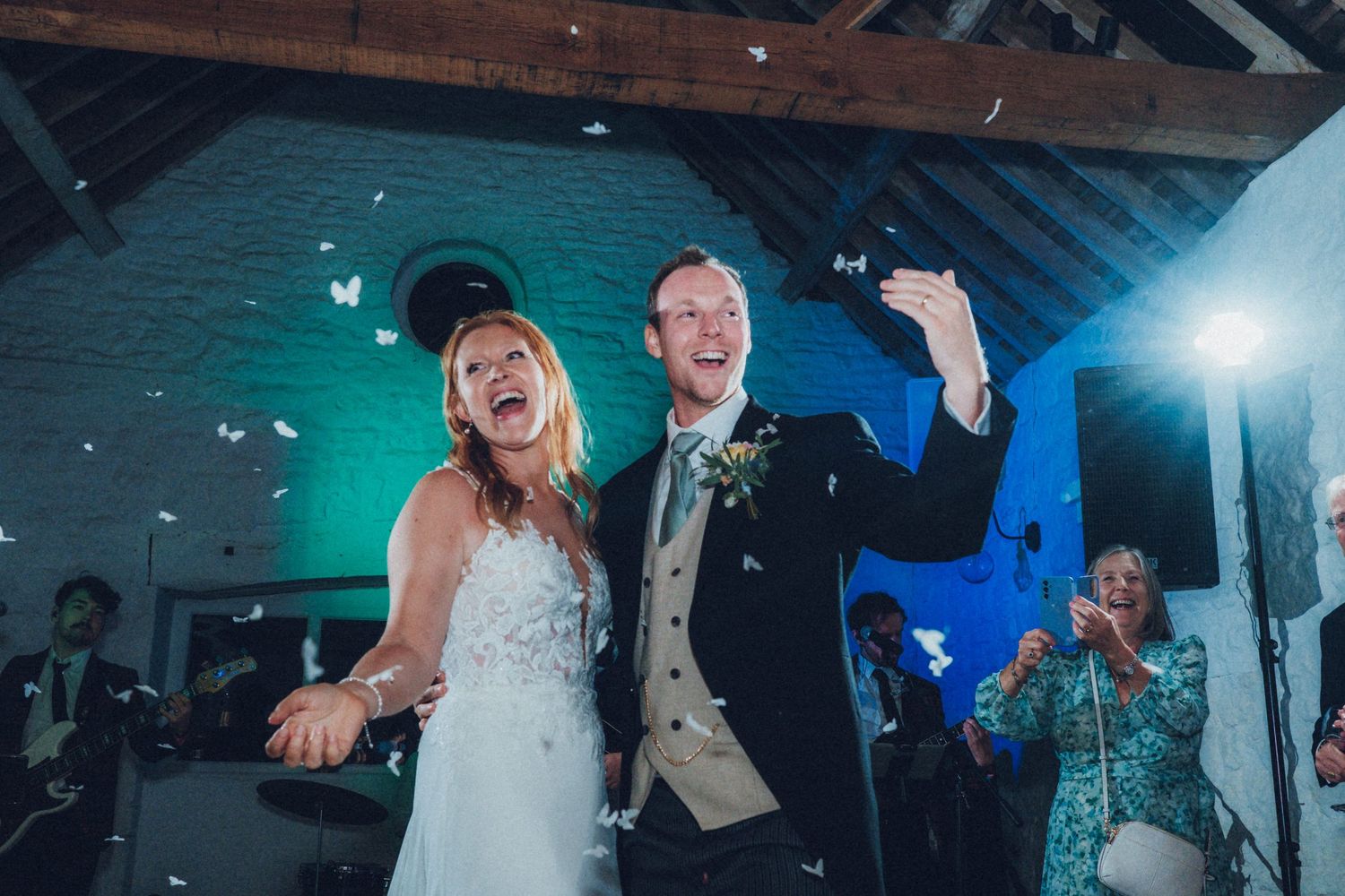 Wedding party dances and celebrates under wooden beams with dramatic lighting.