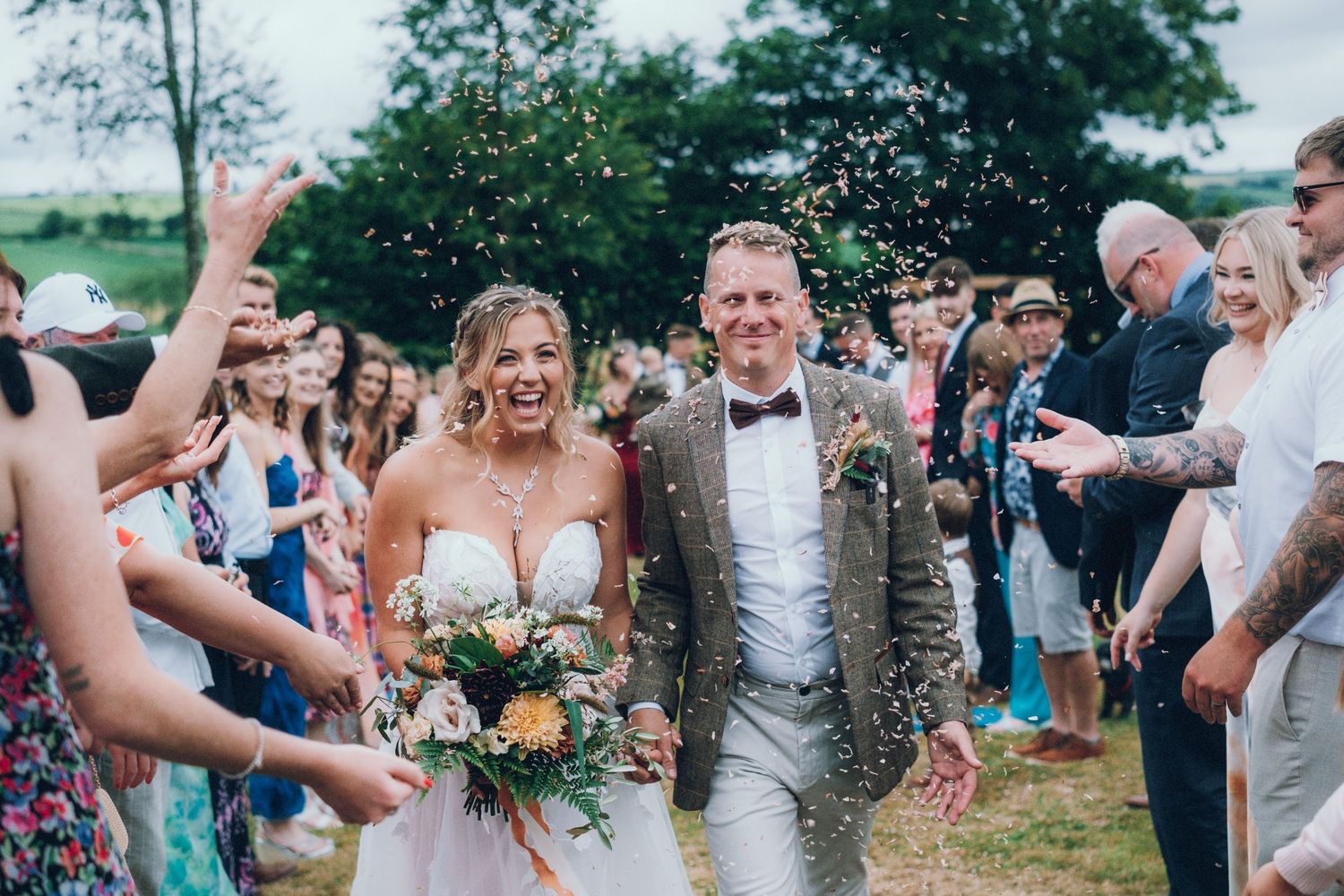 Happy newlyweds celebrate while walking through crowd throwing confetti outdoors.
