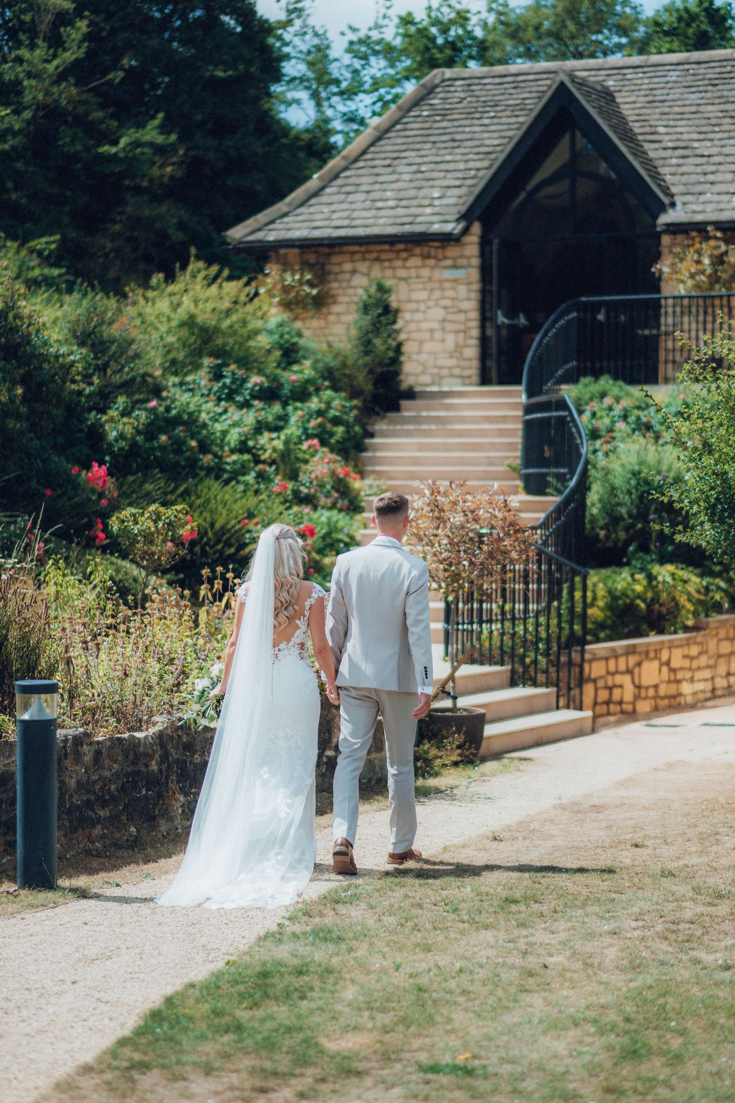 Couple walks towards rustic brick building surrounded by garden landscaping.