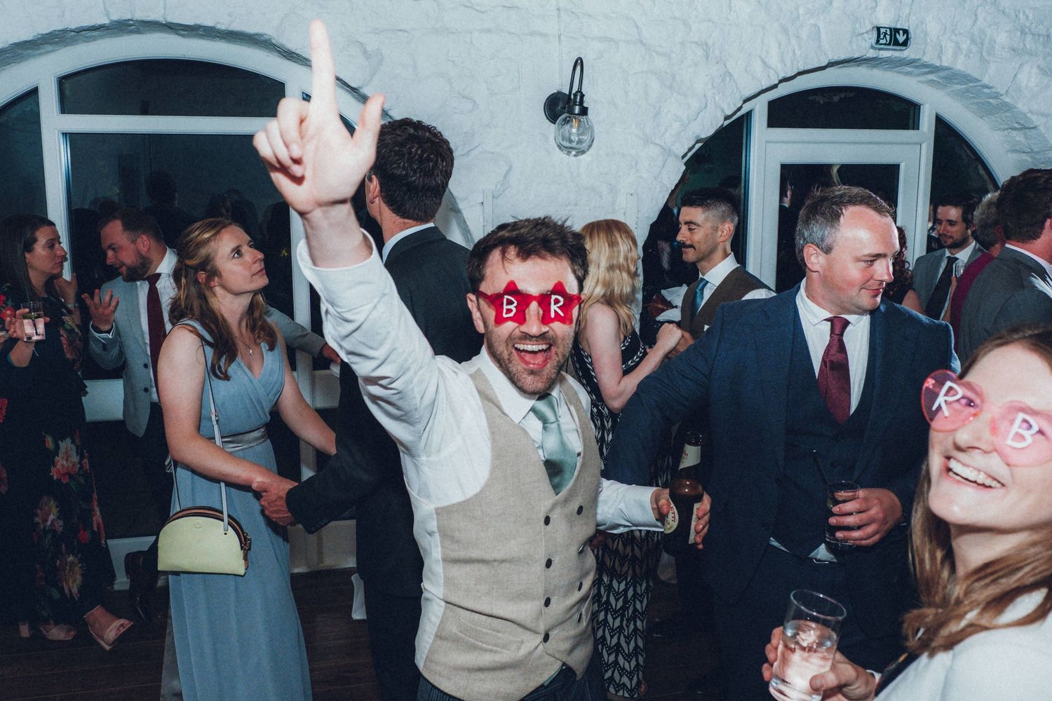 Guests celebrate on a packed dance floor at an indoor wedding reception.