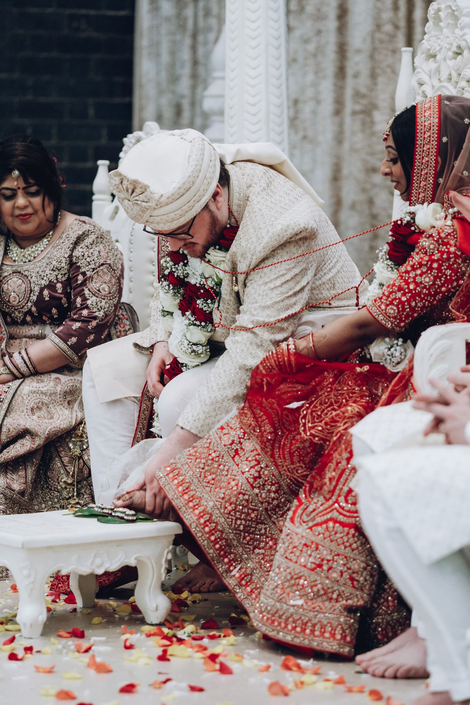 Traditional Indian wedding ceremony with participants in ornate red and cream attire seated on floor.