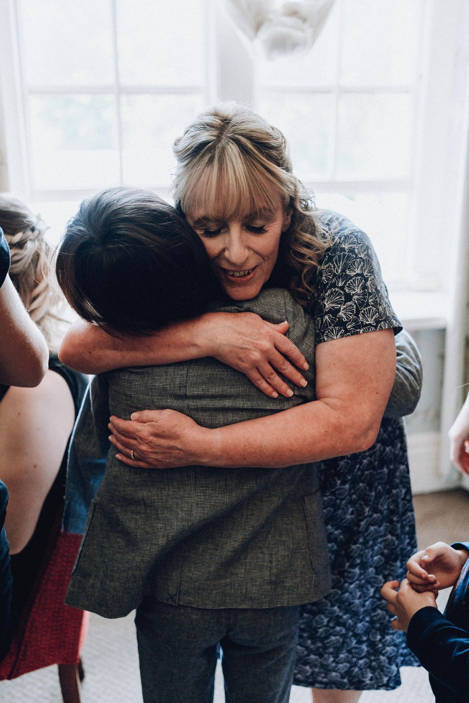 Group of people embracing in a warm hug at an indoor gathering with white curtains.