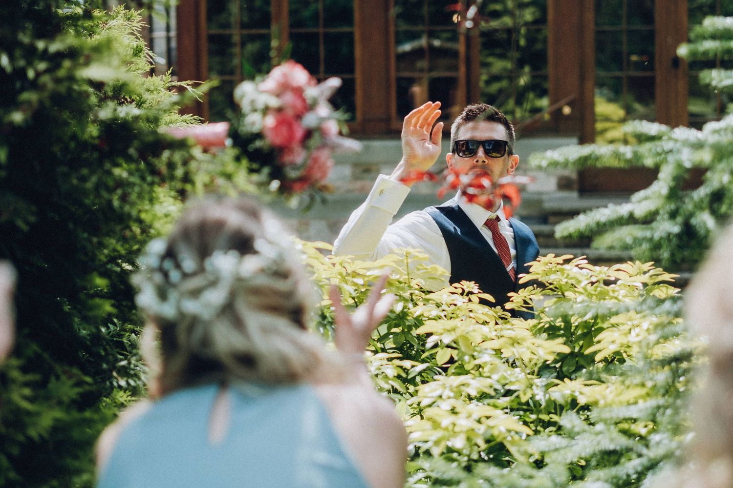 Wedding guests mingle in a lush garden setting with flowering plants and trees.