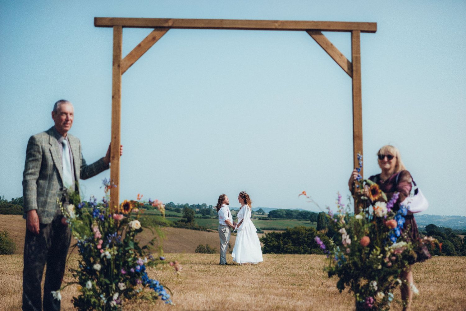 A wooden wedding arch decorated with flowers stands against a blue sky.