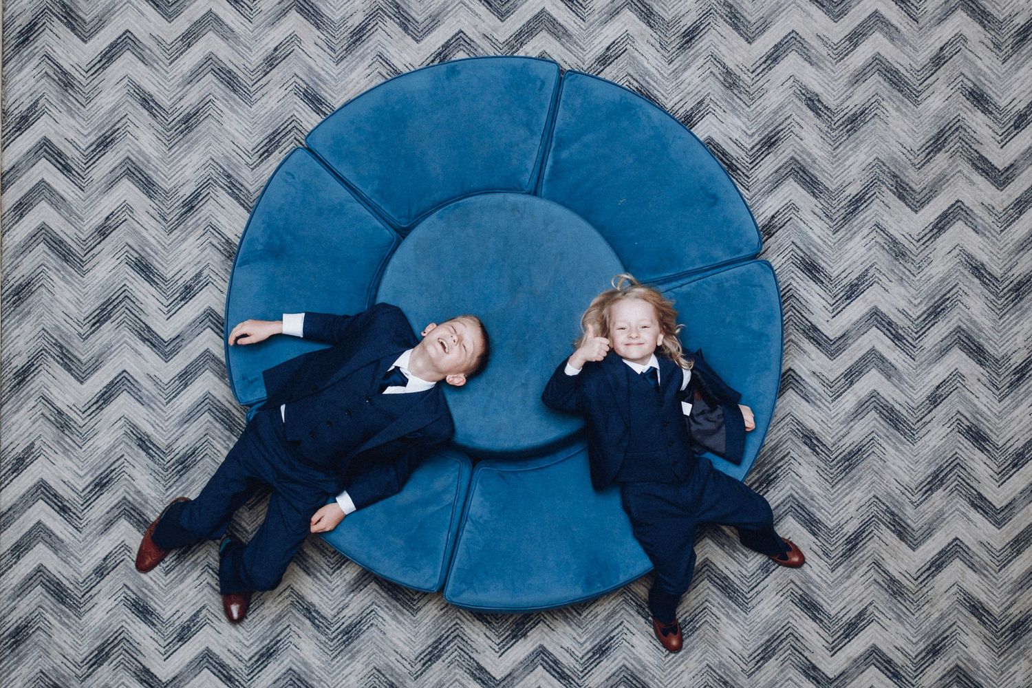 Groomsmen lying on a chevron patterned blue carpet in formal suits.