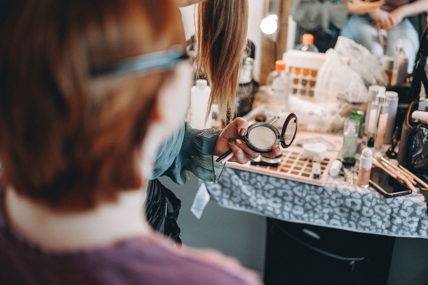 Makeup products and cosmetics arranged on a vanity table with mirror lighting.