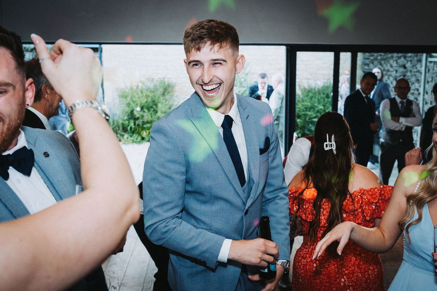 Guest in light blue suit celebrating at indoor wedding reception.
