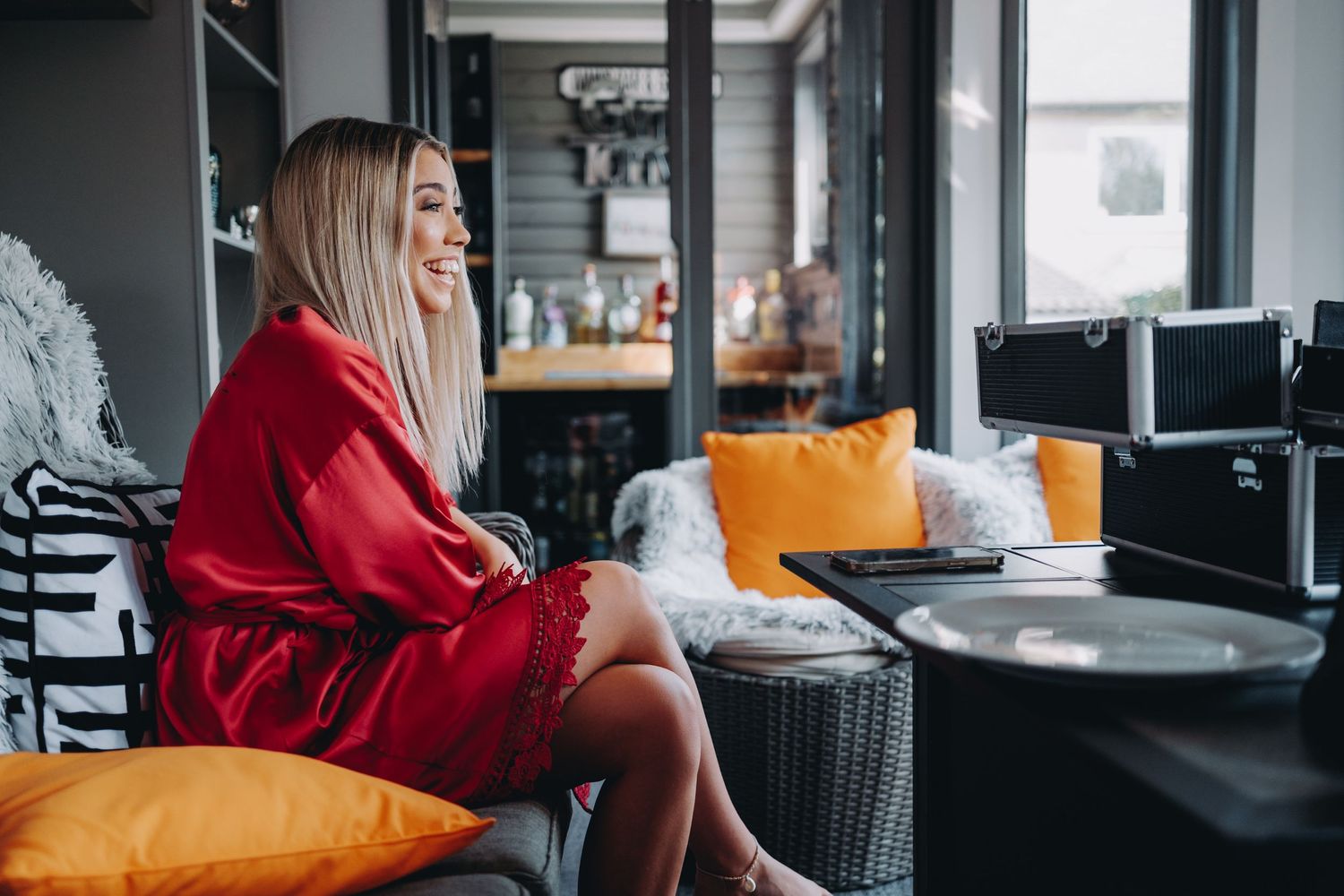 Woman in red robe relaxing on modern furniture with orange accent pillows.