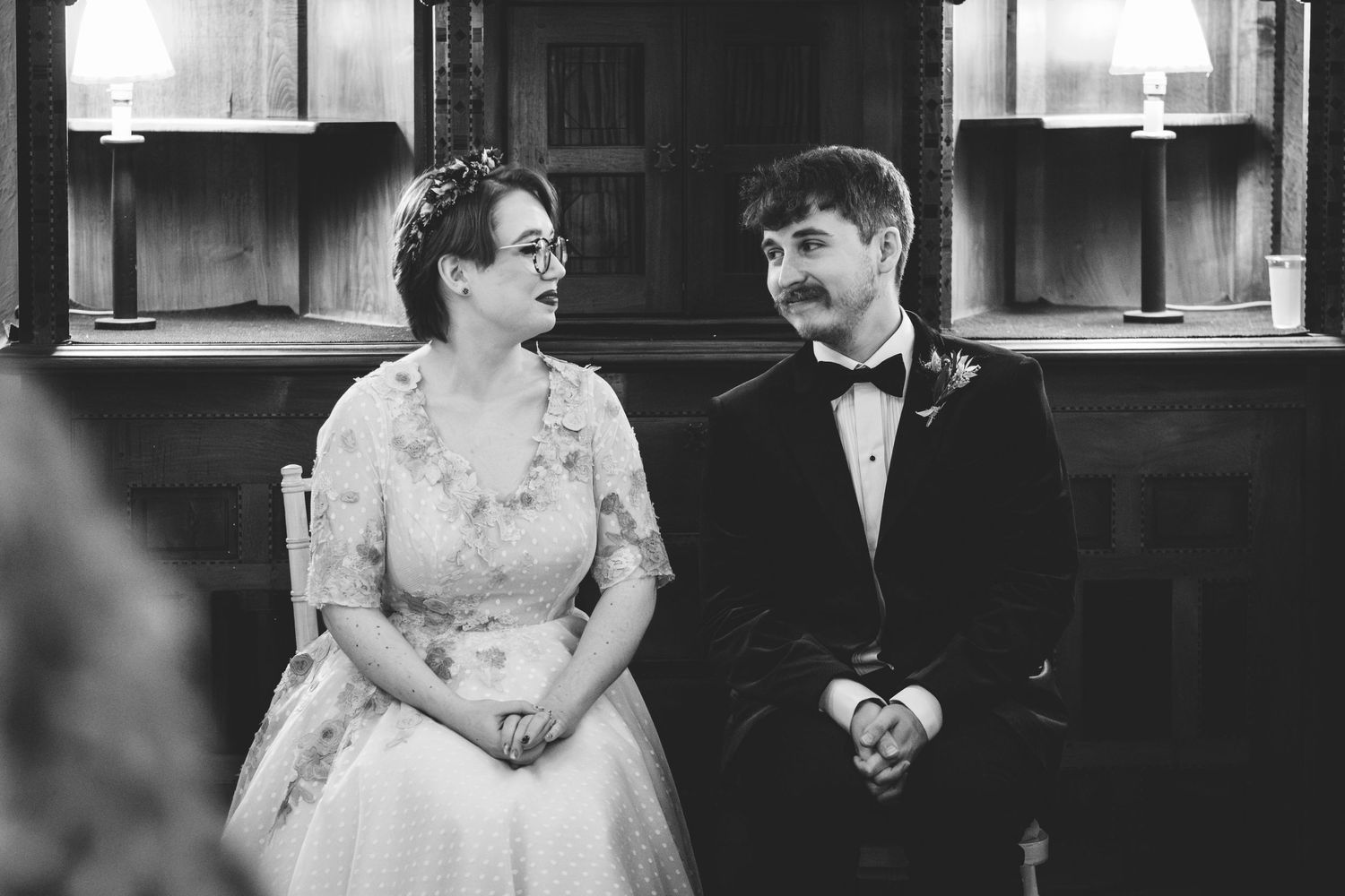 A couple sits together during their vintage-style wedding ceremony in formal attire.