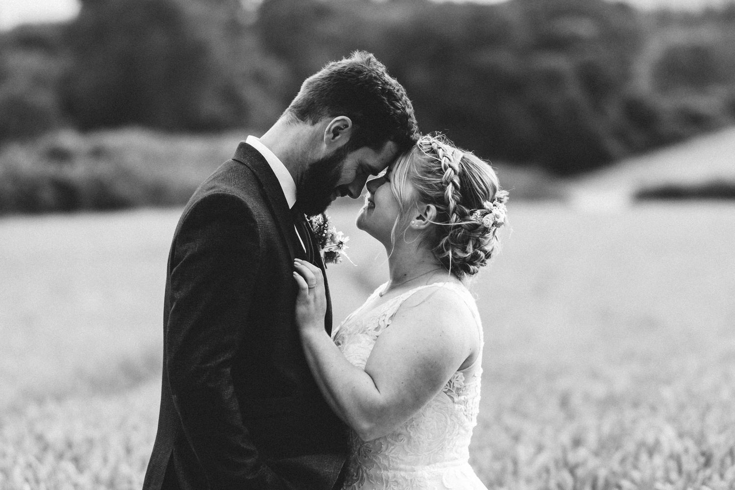 A black and white intimate portrait of a couple sharing a romantic moment on their wedding day in a field.