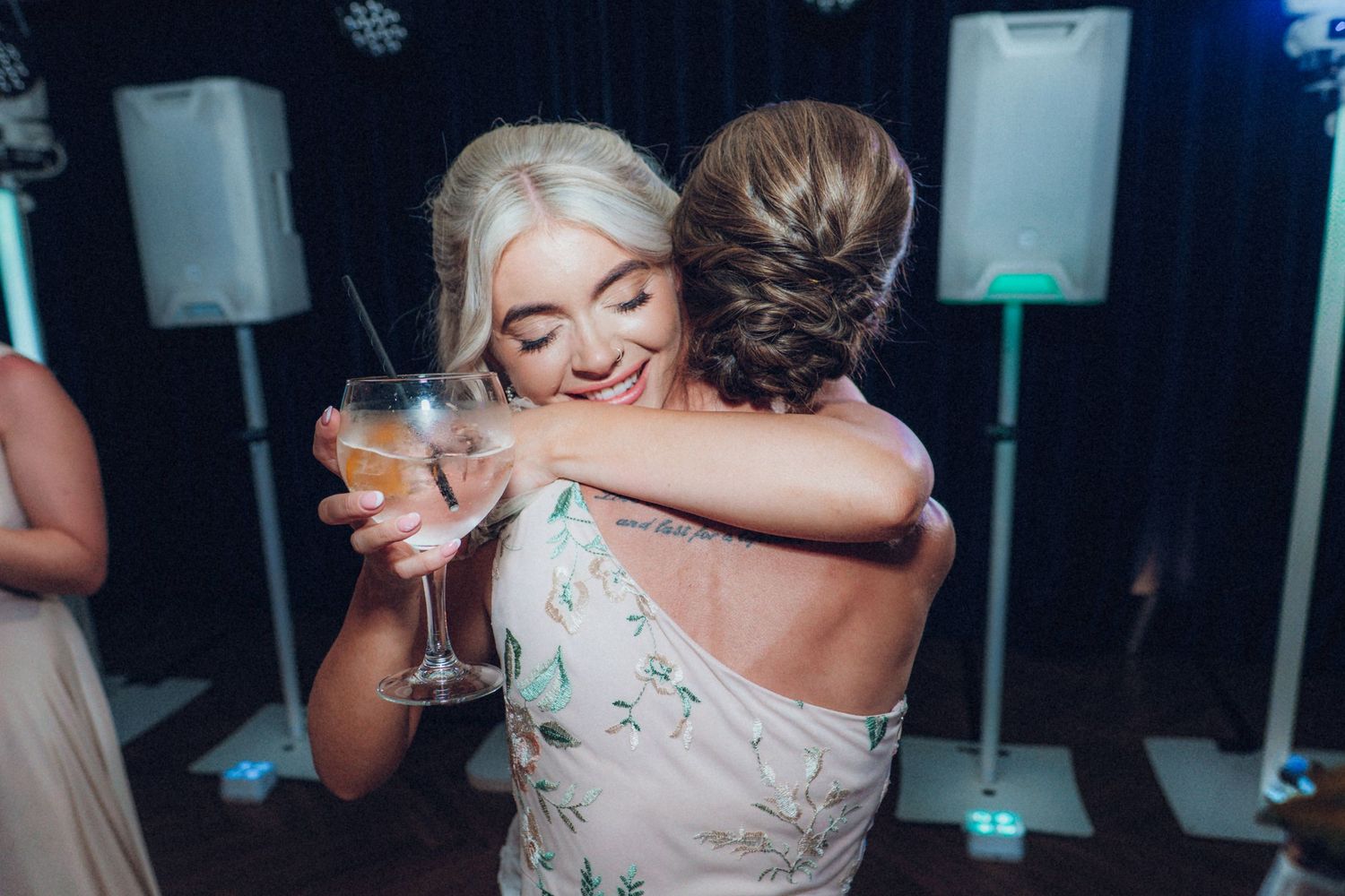 Wedding guests embracing on dance floor during evening reception celebration.